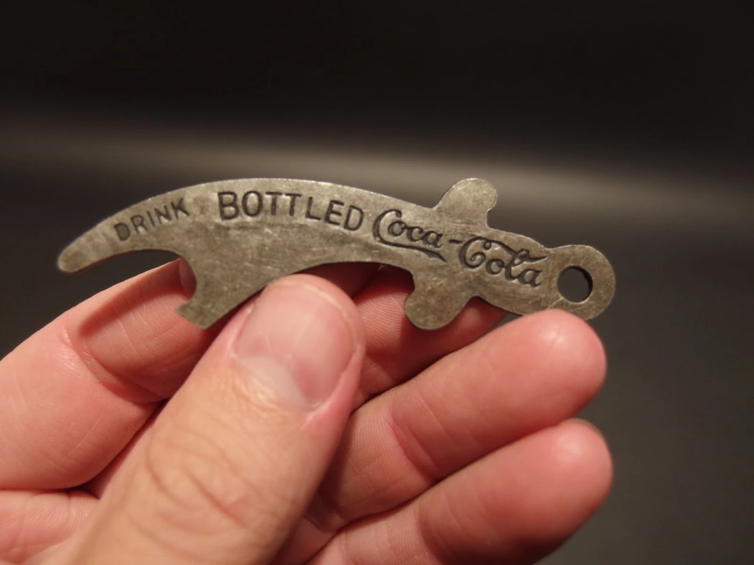 Coca Cola Bottle Opener: Title:Coca Cola Bottle OpenerDescription:3" Long Nice reproduction coca cola bottle opener shaped like a pirate sword I believe. It says Drink Bottled Coca Cola on one side then "Purity is sealed in