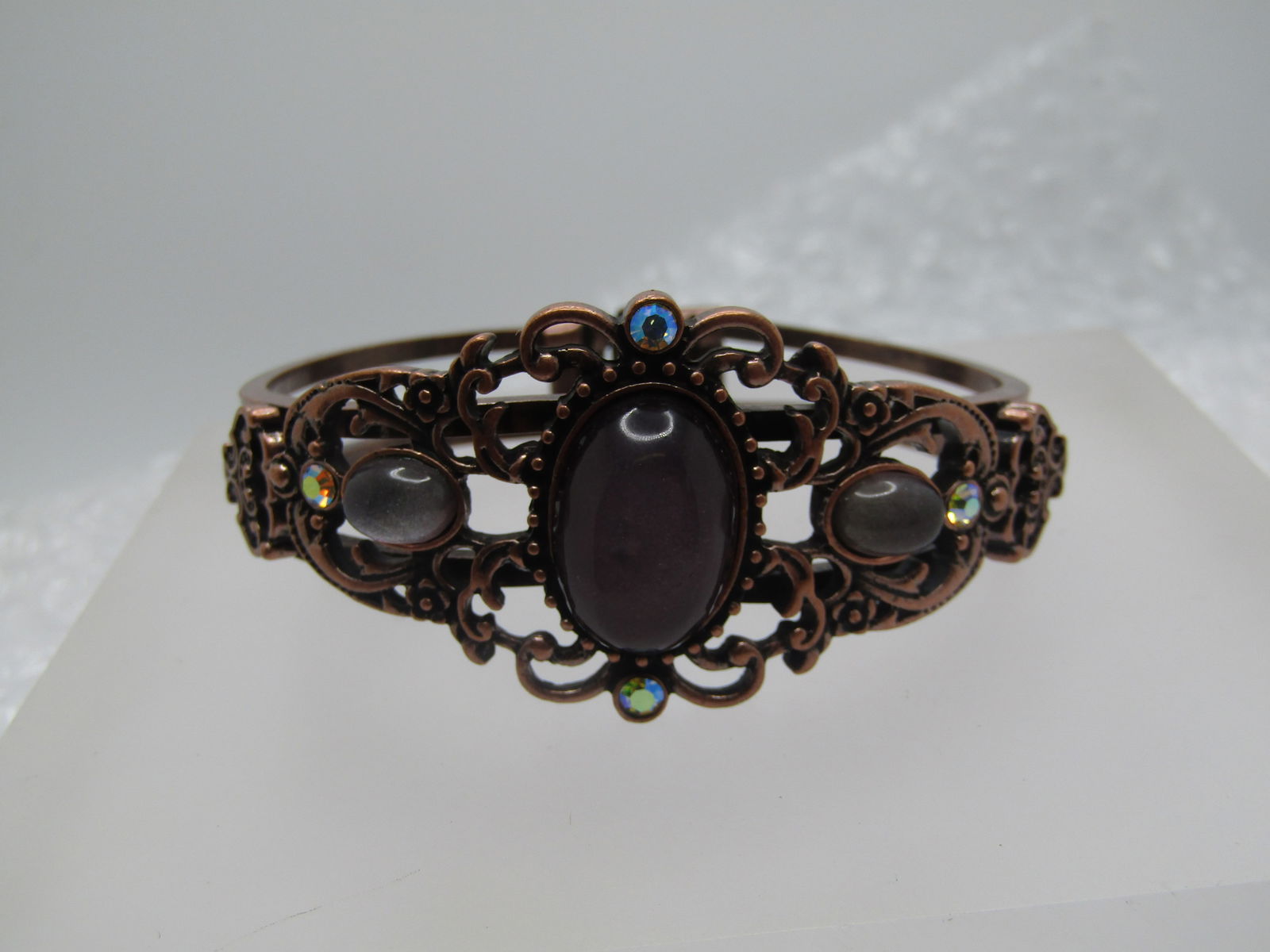 Vintage Purple & AB Hinged Clamper Bracelet, Copper Tone, 6.75": Vintage Purple & AB Hinged Clamped Bracelet, Copper Tone, 6.75". This has a filigree scrolled top with lucite cabochons in amethyst and silvery tond colors and four aurora borealis rhinestones. It is