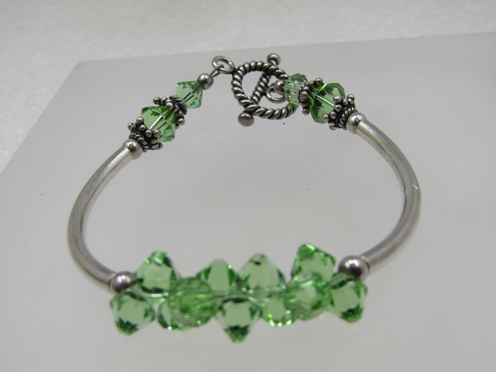 Sterling Green Crystal Toggle Bracelet, 6.75": Sterling Green Crystal Toggle Bracelet, 6.75". This as two curved sterling tubual sections to the bracelt with a ridged toggle clasp and ring with a few beaded accents. There are three sections of lig
