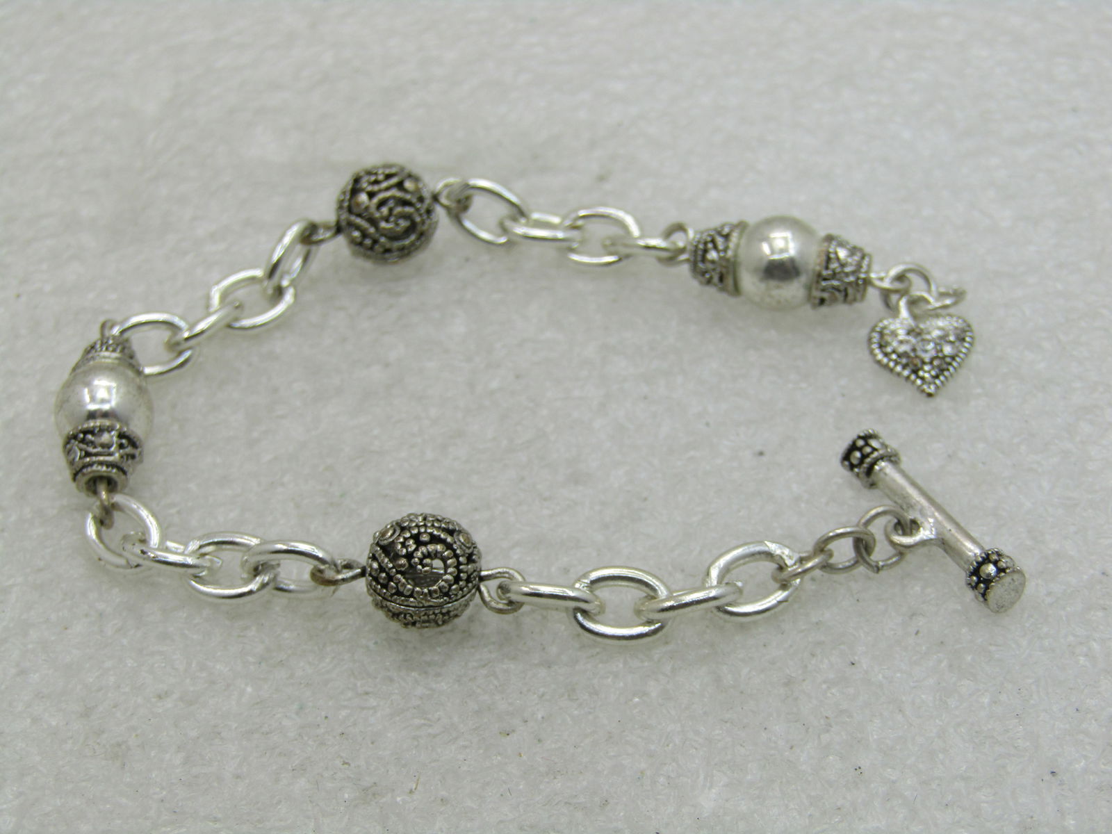 Silver Beaded Bracelet Rhinestone Heart Charm at Toggle Clasp, 7": Silver Beaded Bracelet Rhinestone Heart Charm at Toggle Clasp, 7" - Bali sort of accents with the fine work around the beads, filigree 7.5mm round beads on a chunky oval link. May have silver plating