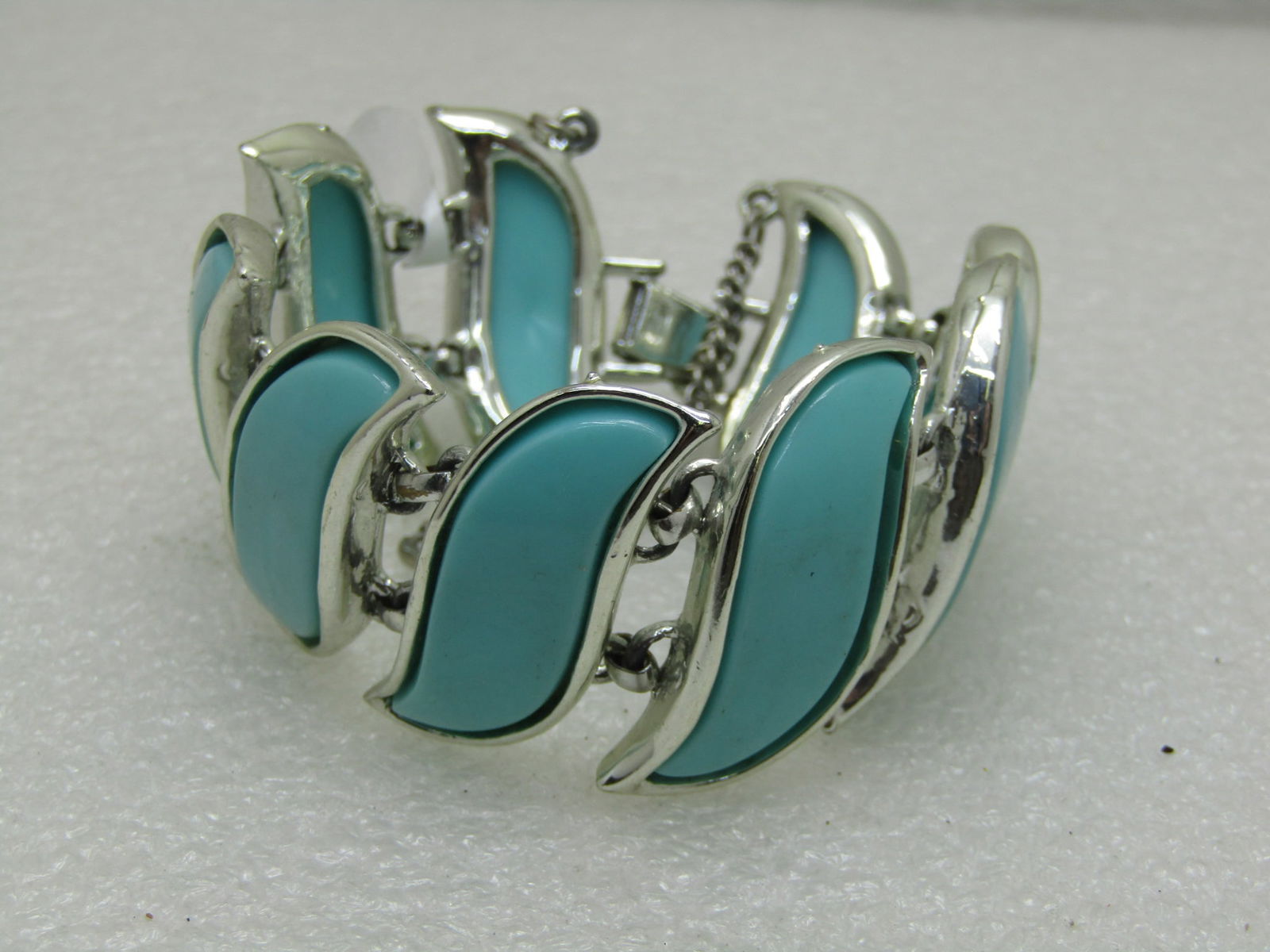 Vintage Teal Lucite Acrylic 1960's Bracelet 7.25": Vintage Teal Lucite Acrylic 1960's Bracelet 7.25". Flip over clasp with safety chain. Appx 1-3/8" wide, 7.25" long. Unsigned by maker. Silver tone metal. Very good vintage condition. Inv.W.6.299.6
