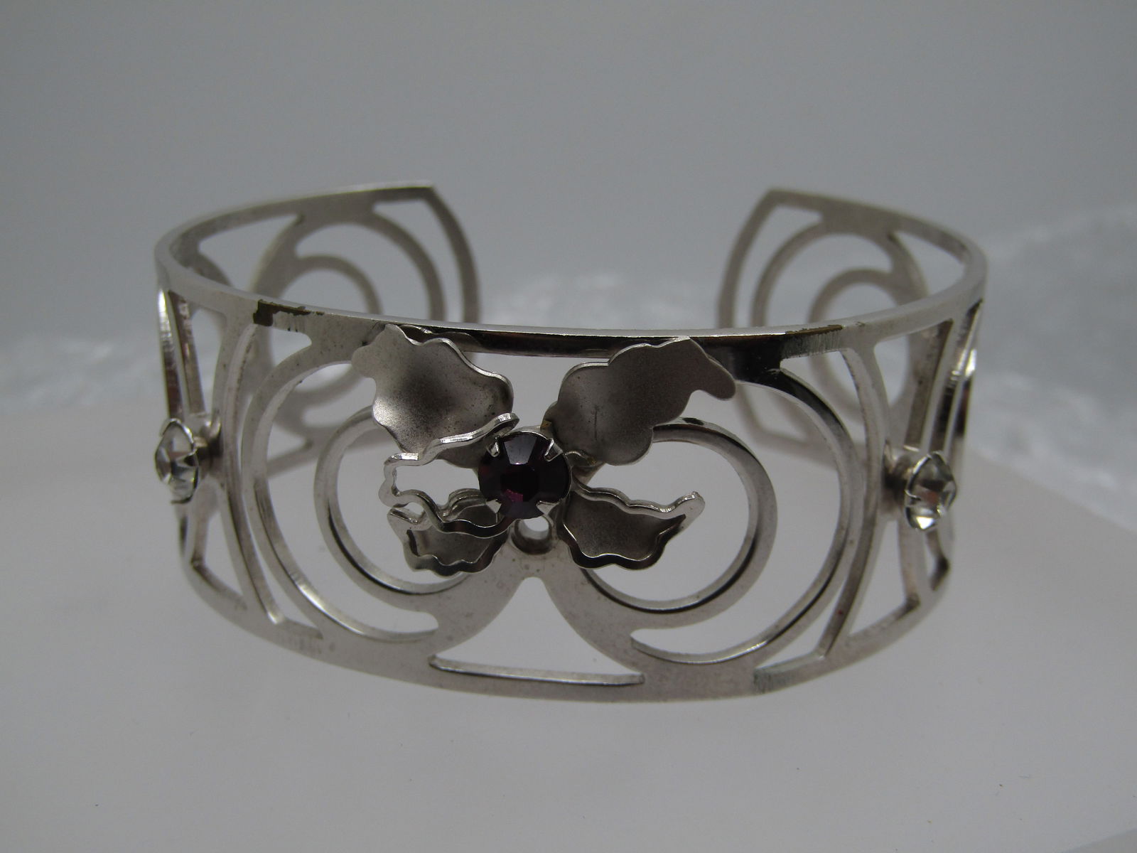 Vintage Silver Tone Orchid Cuff Bracelet, 7", 1960's-1970's: Vintage Silver Tone Orchid Cuff Bracelet, 7", 1960's-1970's. This has two clear stones and a pruple rhienstones that sits in the center of the orchid. It has a scrolled design. It is 1" wide and has e