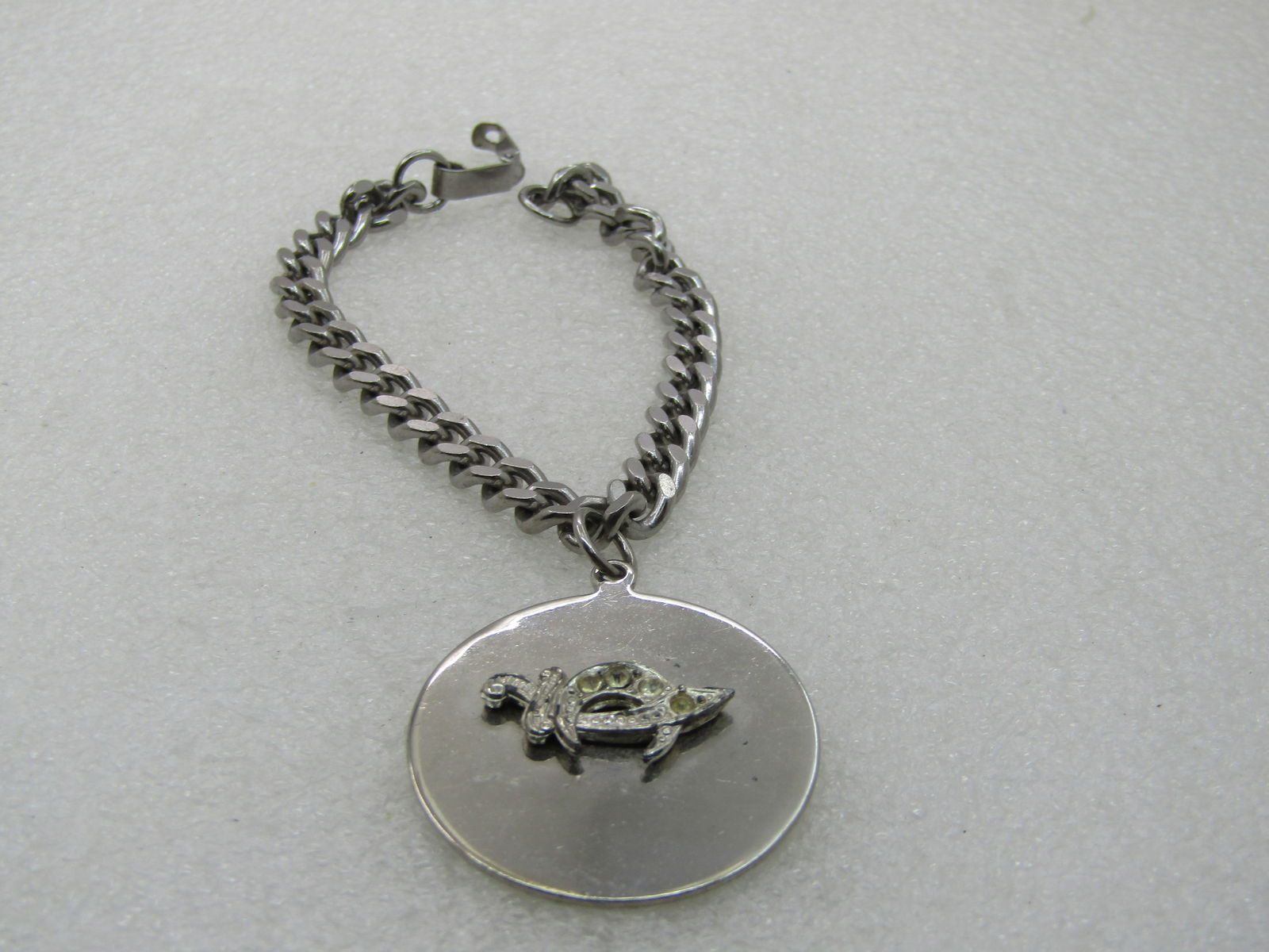 Vintage Shriner's Rhinestone Saber Charm Bracelet, 7", Stainless: Vintage Shriner's Rhinestone Saber Charm Bracelet, 7", Stainless Steel. 6mm wide chuky curb link chain with flip clasp. The charm is 1.25" round with a silver tone clear rhinestone saber mounted on