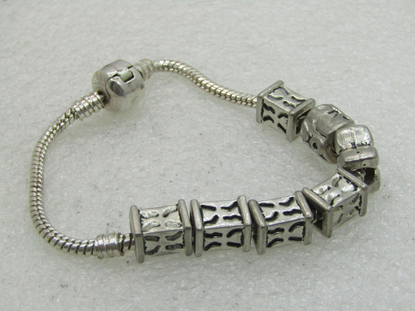 Serpentine Slide Bracelet 3mm wide, 7", Hinged Clasp: Serpentine Slide Bracelet 3mm wide, 7", Hinged Clasp. Silver tone. The beads are square/rectangular beads with cut-out design, butterfly like link and round link. This has a rounded bead-like hinged c