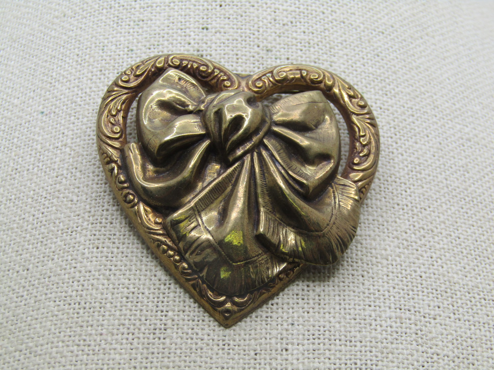 Vintage Heart with Center Bow Brooch, 2.25": Vintage Heart with Center Bow Brooch, 2.25". Brassy gold tone domed brooch with a center bow and scrolled heart frame. It is a somewhat art nouveau style but a 1970's-1980's brooch. It is not