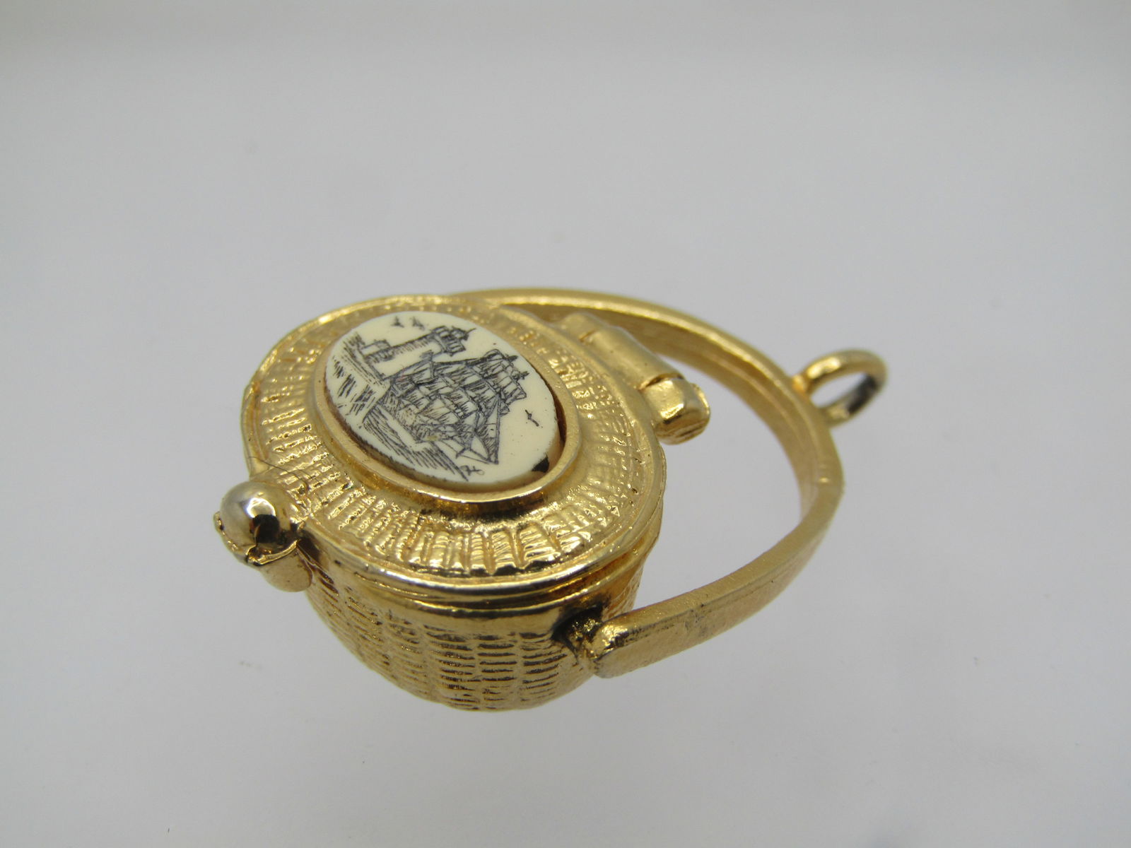 Vintage Scrimshaw Basket Pendant, 1980's-1990's, 1.25": Vintage Scrimshaw Hinged Basket Pendant, 1980's-1990's, 1.25" long with swivel handle. It has a scrimshaw type insert raised ont he lid with a lighthouse and tall ship and gulls. Woven design with