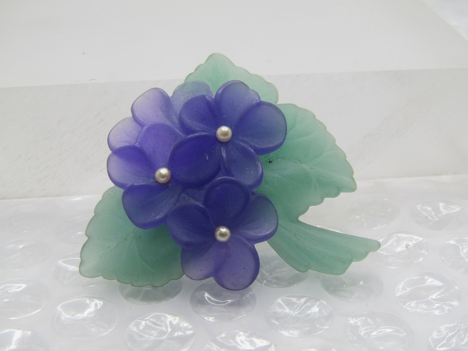 Vintage Avon Violets Brooch, 2" by 1.75", 1970's-1980's: Vintage Avon Violets Brooch, 2" by 1.75", 1970's-1980's. Signed Avon. Each of the full three blossoms you see have a seed pearl in the center of the blossom with three leaves and stems in green. 