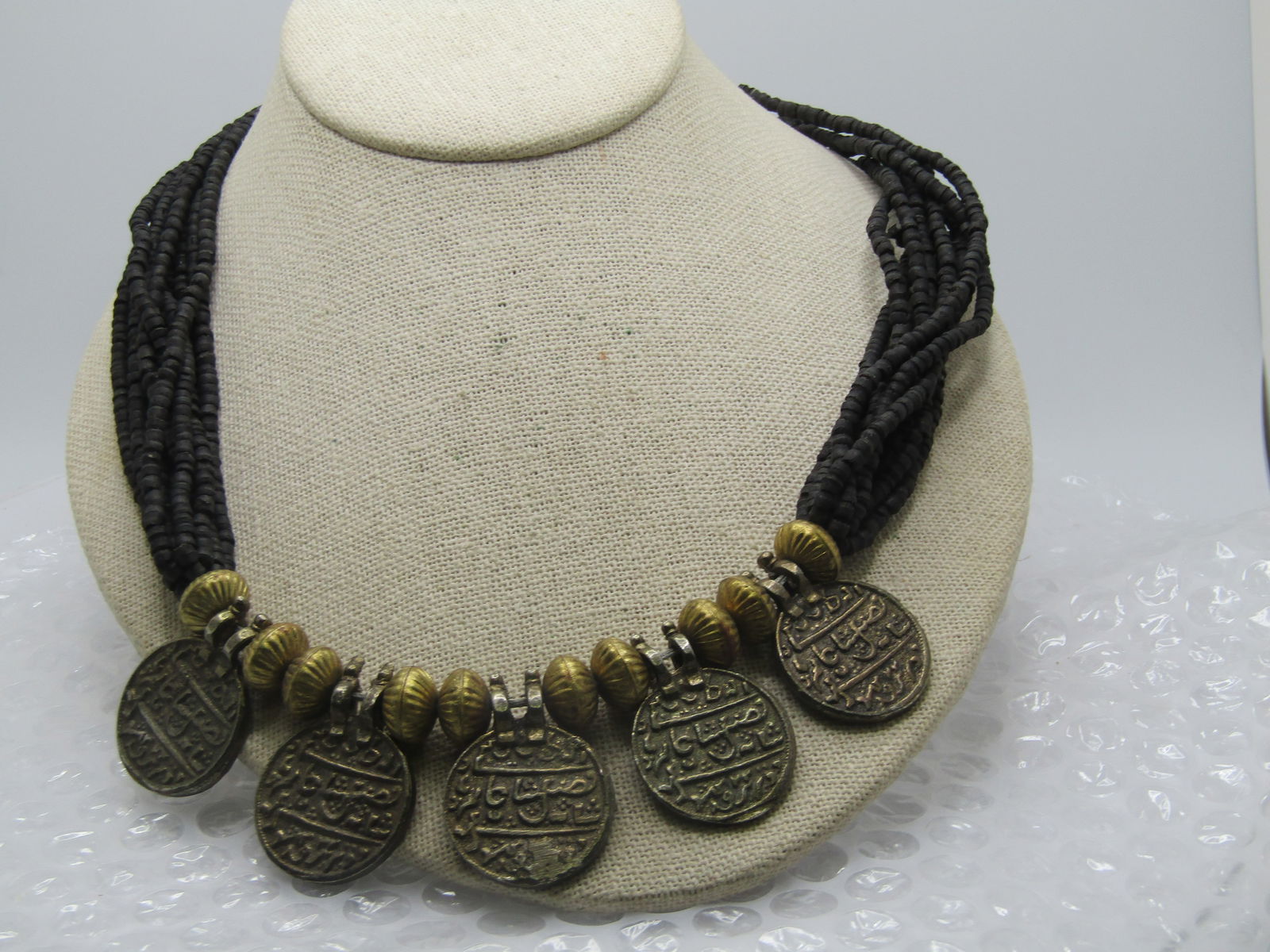 Vintage Mid-Eastern Faux Coin Multi-Strand Necklace, 24". Tribal/Ethnic: Vintage Mid-Eastern Faux Coin Multi-Strand Necklace, 24". Tribal/Ethnic. It has five rustic faux coins that drop at the bottom with Mid-Estern markings. Appx. 1" wide. Brassy fluted puffy beads are ab