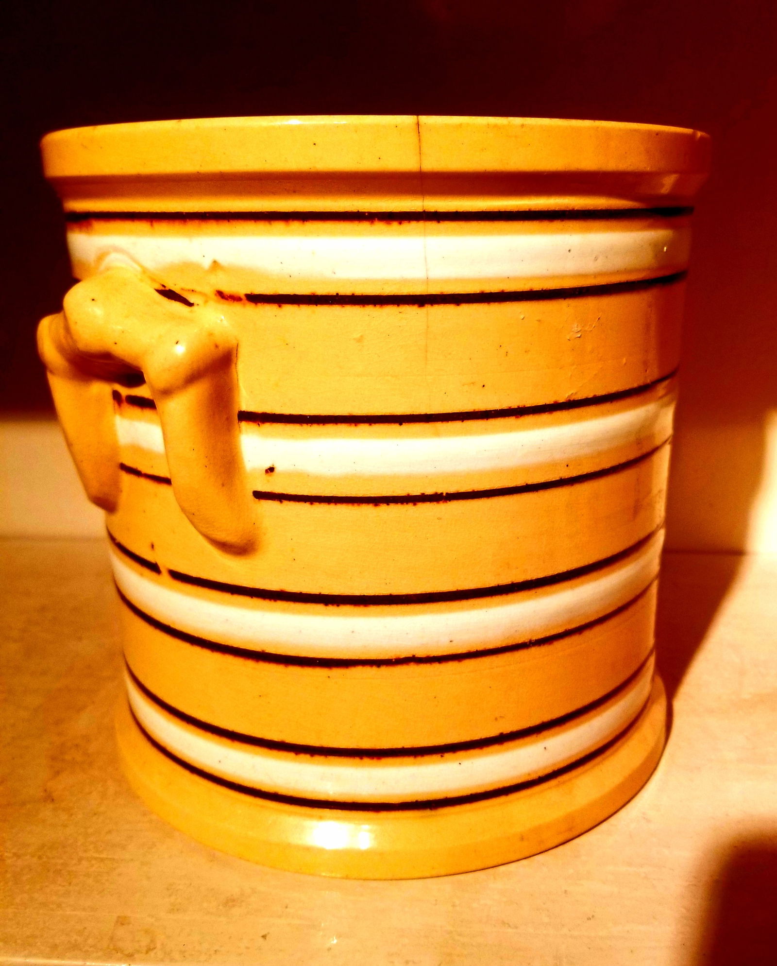 Yellowware jar, brown and white bands: A faint hairline and a few tiny flakes on the rim, both as shown. 7 inches each way. Perfect for utensil storage! C. 1920, English. Shipping:Domestic: Shipping rates are determined