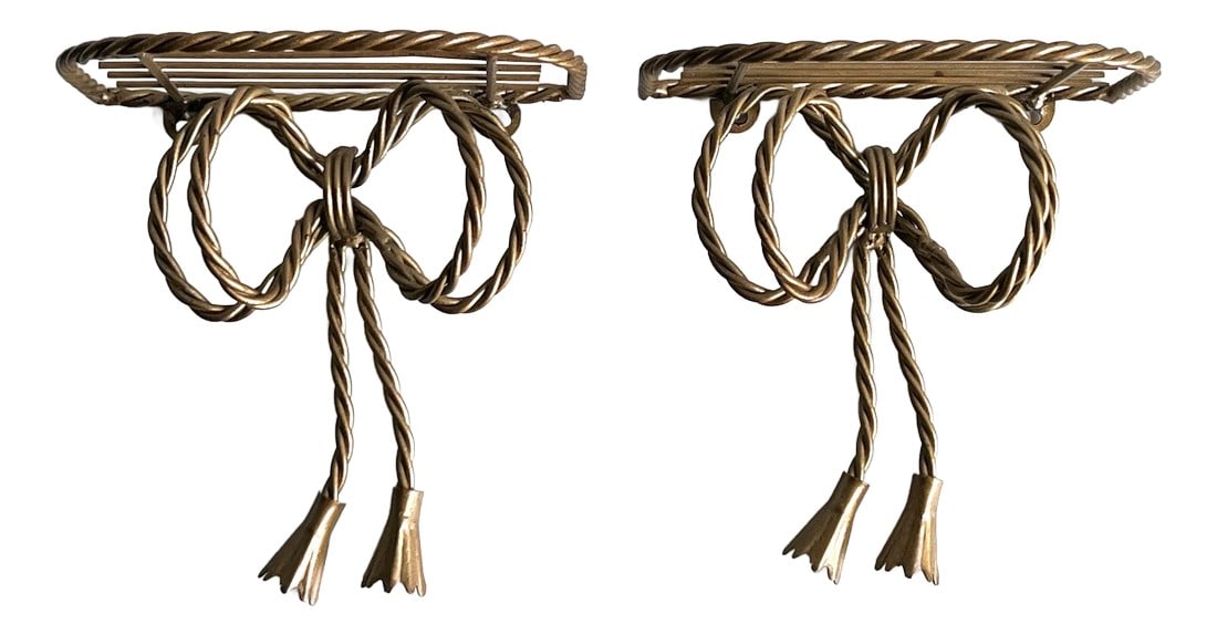 Pair of Vintage Italian Gold Rope Ribbon and Tassel Wall Shelves: Charming and elegant, this pair of vintage patina'd brassy gold tone wall shelves features a sculptural ribbon and tassel motif, evocative of Italian and French neoclassical or Hollywood Regency desig