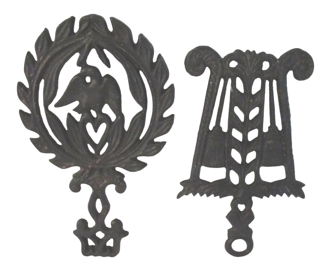 1970s Americana Black Cast Iron Hanging Trivets, a Pair: Vintage pair of black cast iron trivets featuring an Americana theme. One trivet features a wheat broom motif (7.75"L x 4.75"W x .75"H) and the other an eagle in center, (8.5"L x 5.5"W x .75"H).
