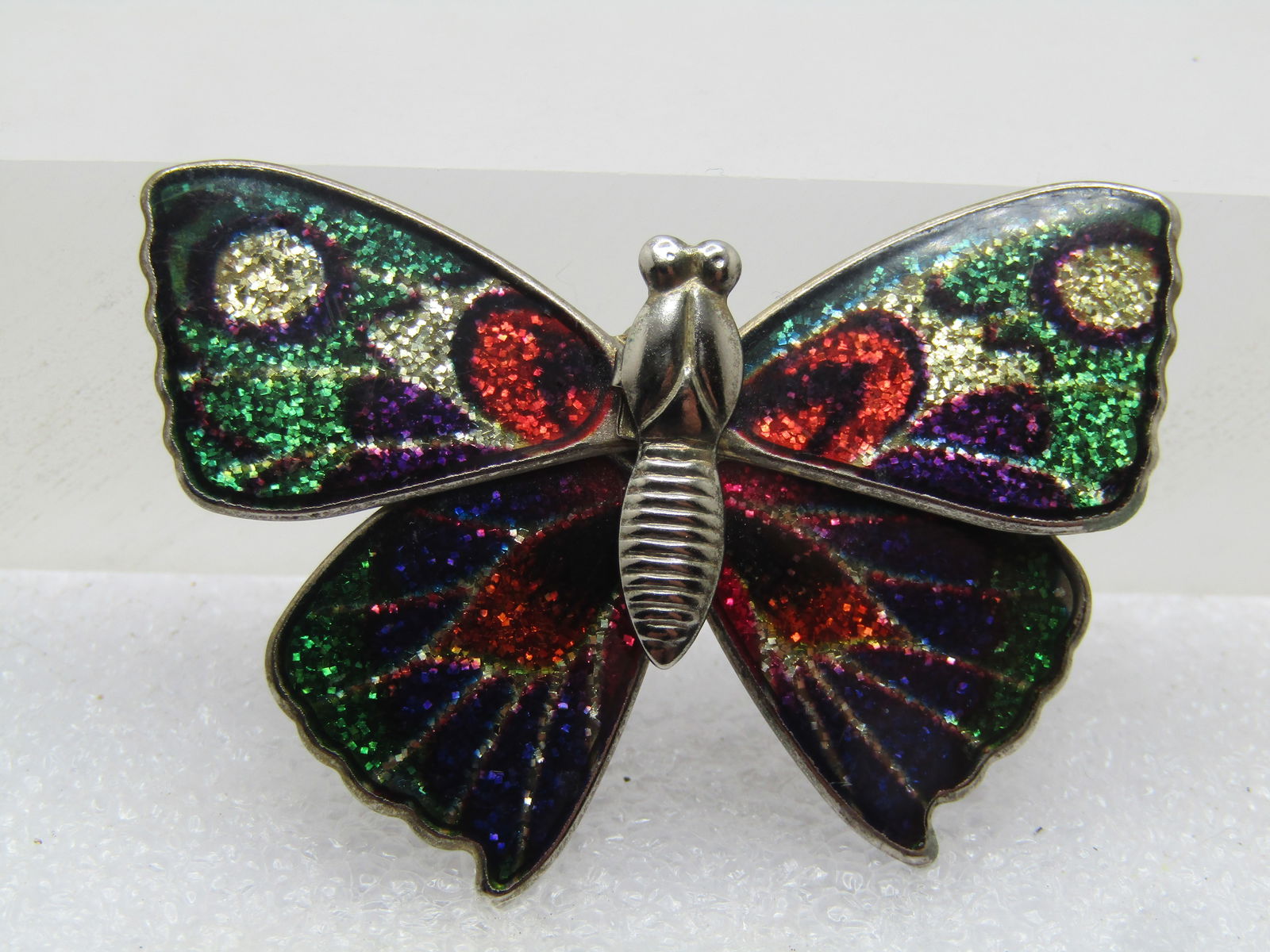 Vintage Glitter Enameled Butterfly Brooch, C-Clasp, 1960's-1970's: Vintage Glitter Enameled Butterfly Brooch, C-Clasp, 1960's-1970's. Gold tone with a gold tone torso and green, blue, red, gold, purple, black glitter enameled wings. It is 2" wide and 1.25" tall. Cost