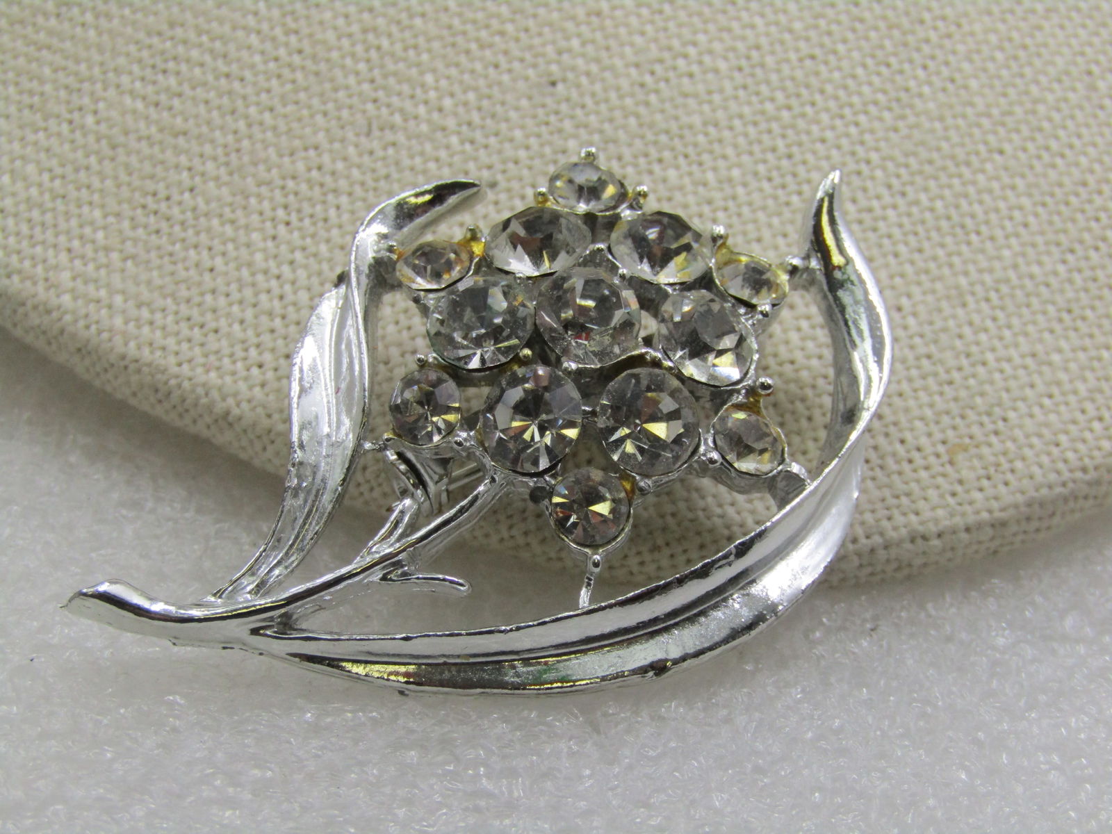 Vintage Rhinestone Floral Brooch, Blossom & Stem, 1940's-1950's: Vintage Rhinestone Floral Brooch, Blossom & Stem, 1940's-1950's. Silver tone metal with two long curved leaves with the center lower than the sides of the leaves, a stem and a center clear rhinestone
