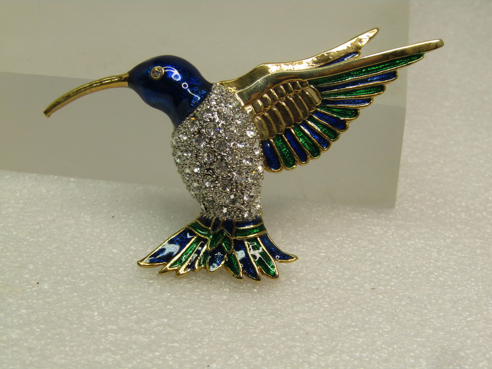 Vintage Enameled Rhinestone Hummingbird Brooch, 1980's-1990's: Vintage Enameled Rhinestone Hummingbird Brooch, 1980's-1990's. Clear rhinestone textured domed body with blue and green enameling and a rhinestone eye - gold tone long beak and wings. Locking clasp. I