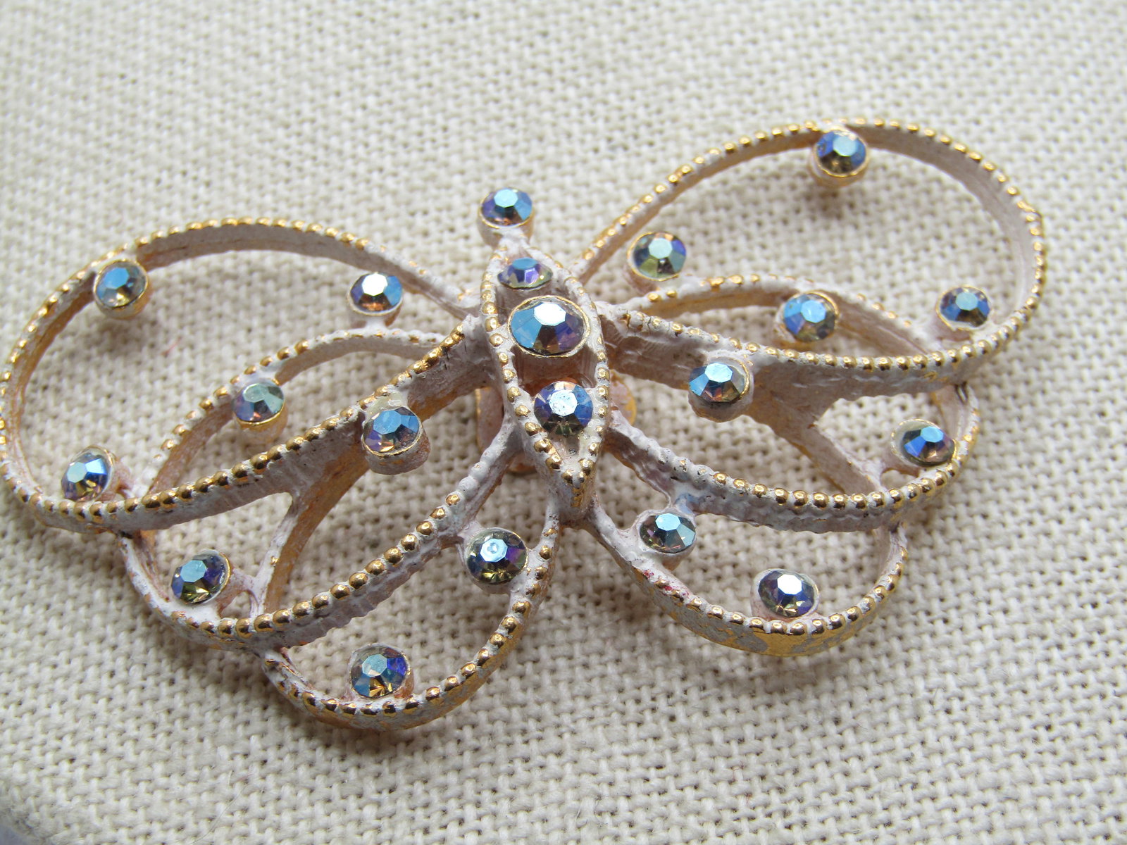 Vintage Rhinestone Butterfly Dress Clip, White Enameling, 1950's-1960's. It is appx. wide and 1.25": Vintage Rhinestone Butterfly Dress Clip, White Enameling, 1950's-1960's. It is appx. wide and 1.25" tall with dotted like gold tone frame washed in white enameling. The rhinetones are blue aurora bore