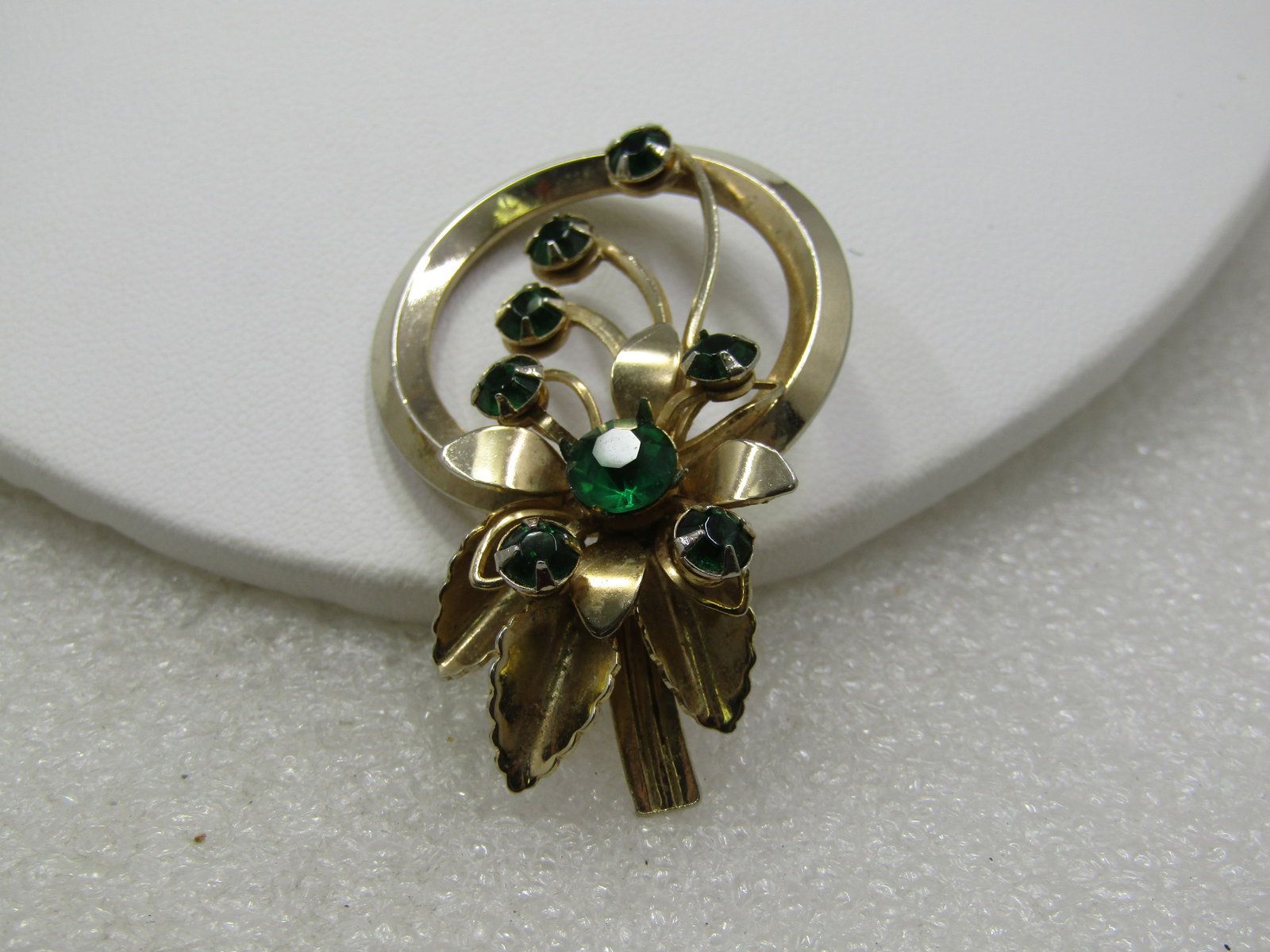 Vintage Rhinestone Floral Brooch 1960's: Vintage Rhinestone Floral Brooch 1960's, nearly 2" tall and 1.25" round. Circle brooch with a blossom and curcling stems passing into the open area of the circle, round green rhinestones accent the br