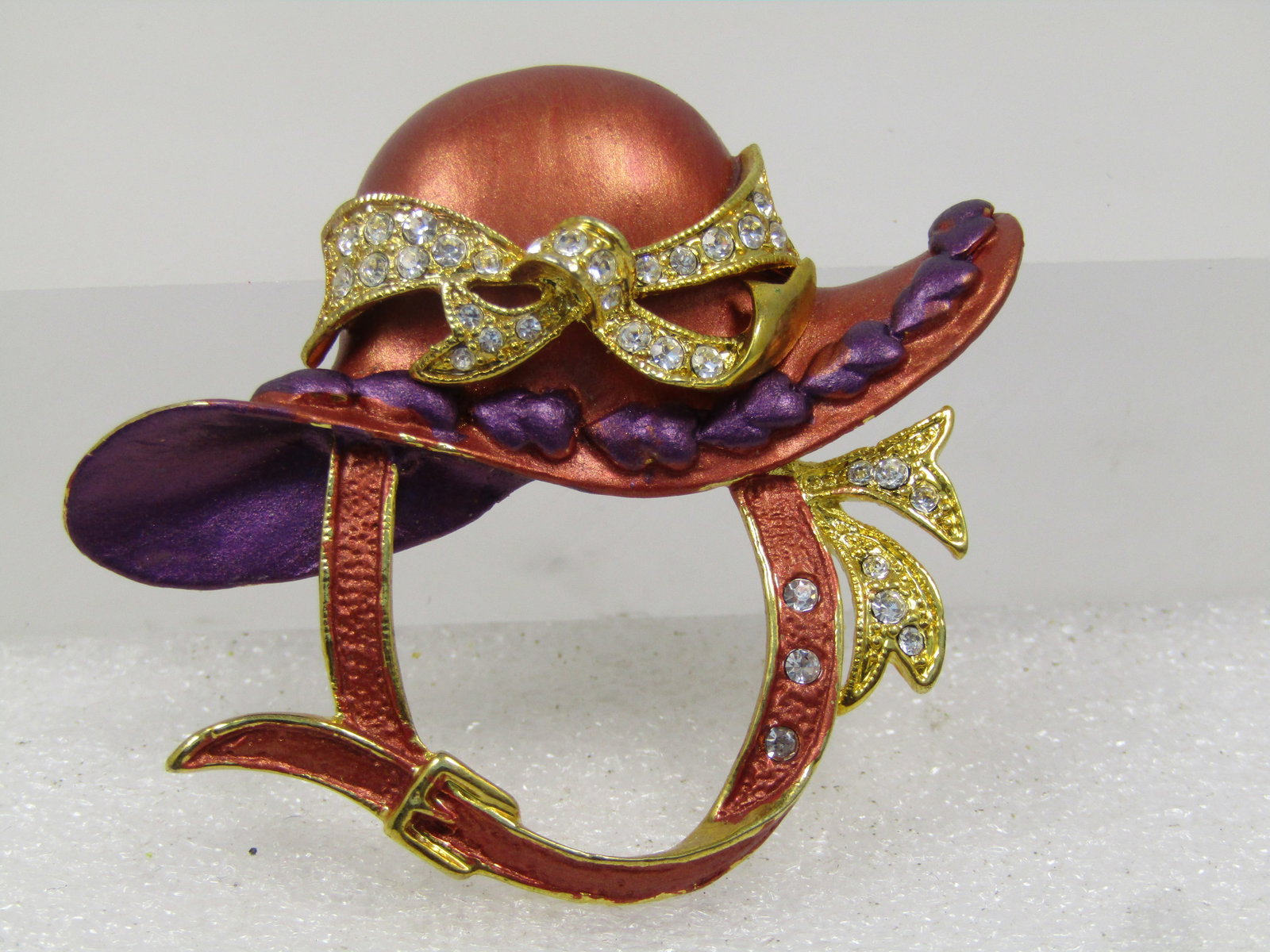 Vintage Enameled Red Hat Brooch, Purple & Rhinestone Accents, 1990's: Vintage Enameled Red Hat Brooch, Purple & Rhinestone Accents, 1990's. Gold tone with a chin strap and rhinestone bow and purple accents raised on the brim and the inside of the hat purple as well and