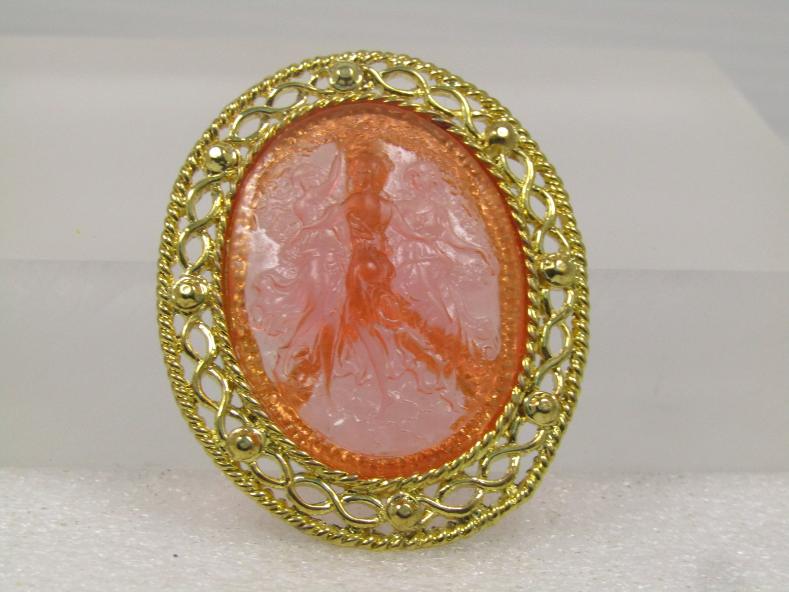 Vintage Pink Three Maidens Cameo Stlye Brooch, Pink, Translucent, 1960's: Vintage Pink Three Maidens Cameo Stlye Brooch, Pink, Translucent, 1960's. It has a gold tone open style frame with gold tone trails that crisscross around the brooch. It is appx. 2-1/8" tall and 1.75"