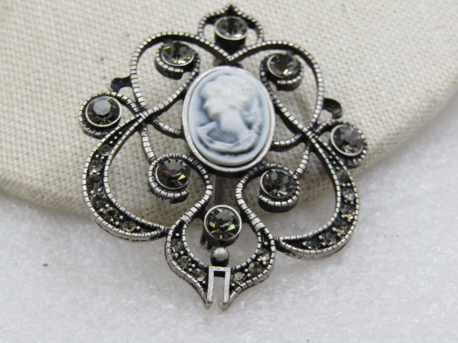 Vintage Rhinestone & Cameo Scrolled Brooch, 2.25": Vintage Rhinestone & Cameo Scrolled Brooch, 2.25" tall and 1.75" wide. It has a faux Wedgwood cameo oval in the top slightly higher than center with eight bezel-set 5mm smoky faceted rhnestones and sm