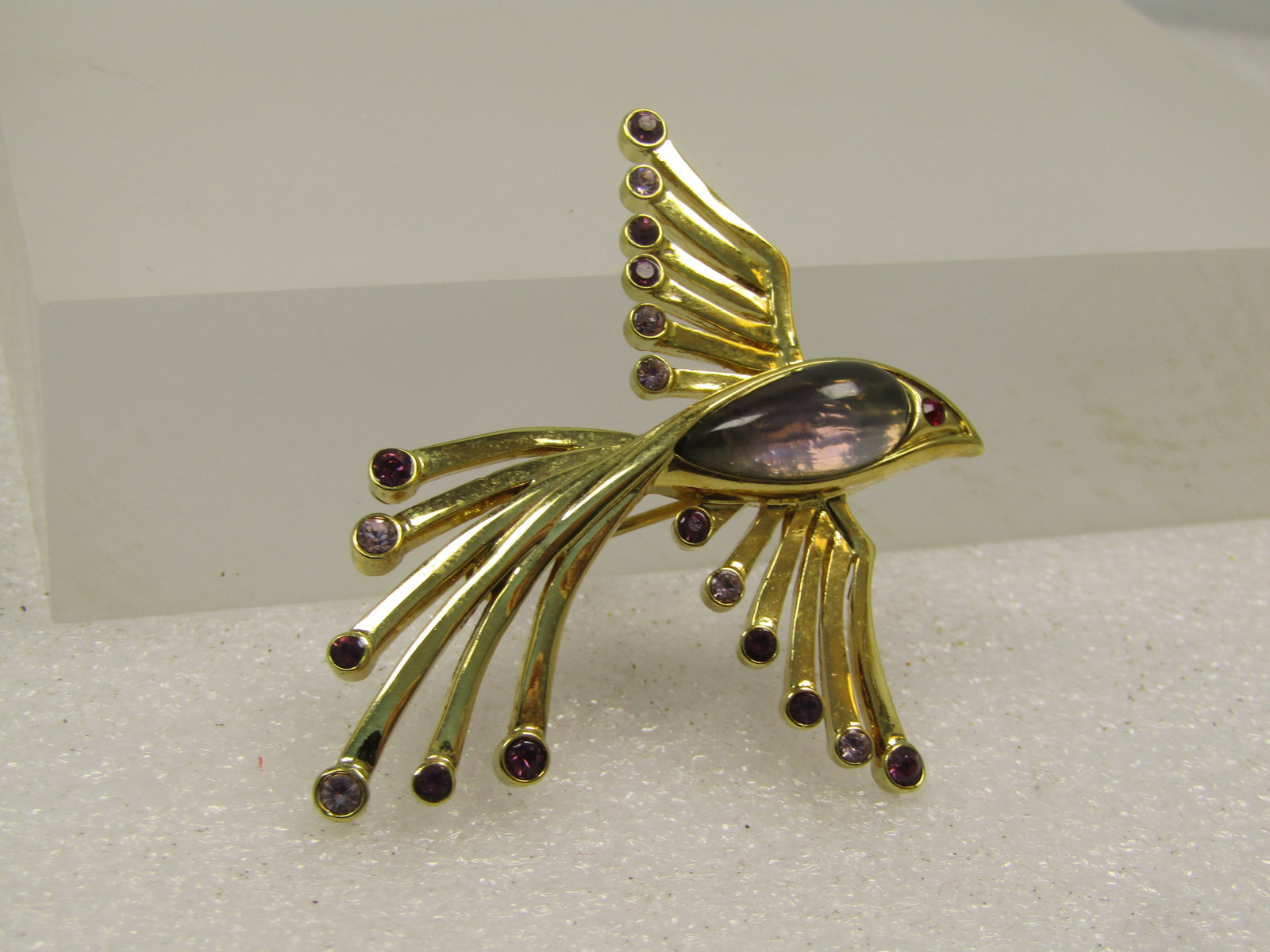 Vintage Bird in Flight Brooch With Rhinestones, 1970's-1980's: Vintage Bird Brooch With Rhinestones, 1970's-1980's. This is gold tone with rhinestones set in the tips of the wings and tail and a lucite elongated pear-shaped domed stone in the body with a red rhin