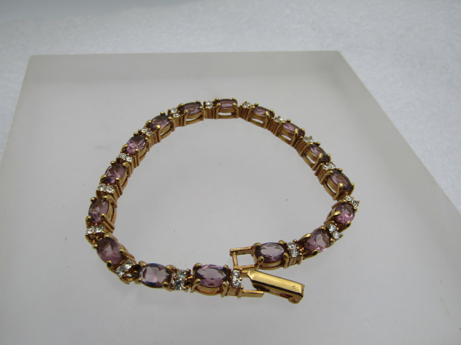 Simulated Amethyst Diamond Tennis Bracelet, 7", Signed Avon: Simulated Amethyst Diamond Tennis Bracelet, 7", Signed Avon. Gold tone and appx. 4.5mm wide. Flip clasp. The stones are a purple glass that are appx. 5.5mm by 4mm. There are two appx. 2.5mm round