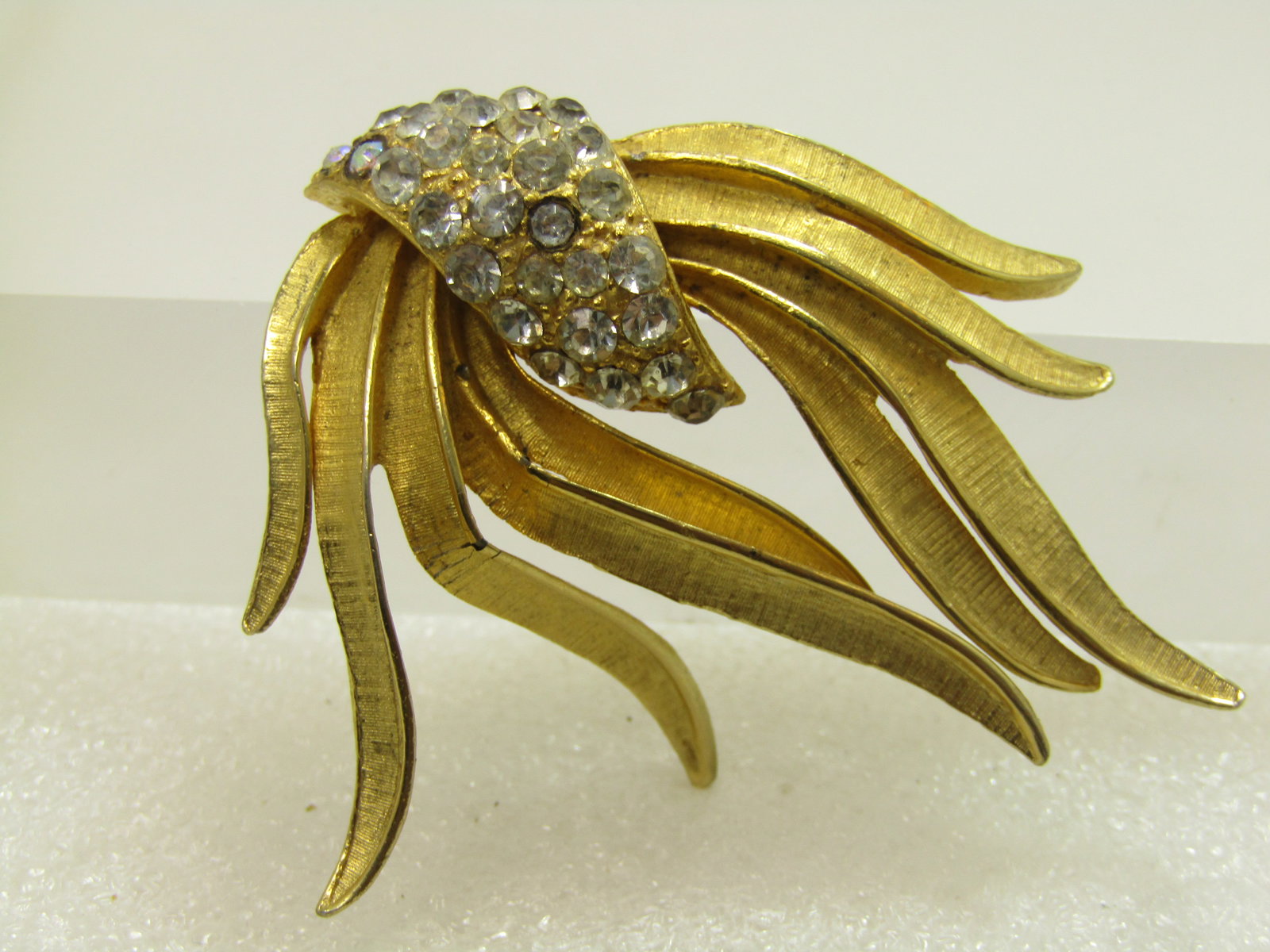 Vintage Clear Rhinestone Swag Brooch, Gold Tone, 1970's: Vintage Clear Rhinestone Swag Brooch, Gold Tone, 1970's. This is appx. 2" tall and wide. with a textured finish to the pieces of the swag with smooth and shiny edges. There is a raised textured
