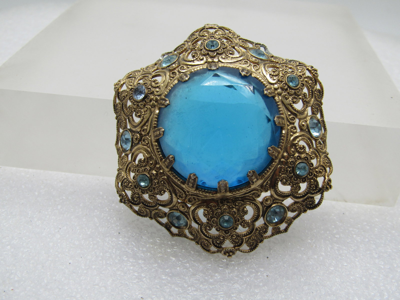 Vintage Filigree Blue Rhinestone Brooch, 1940's-1960's.: Vintage Filigree Blue Rhinestone Brooch, 1940's-1960's. Large Blue 25mm round blue glass tone set with many prongs and a tappering curved lacey scrolled frame around that large stone, The center is ra