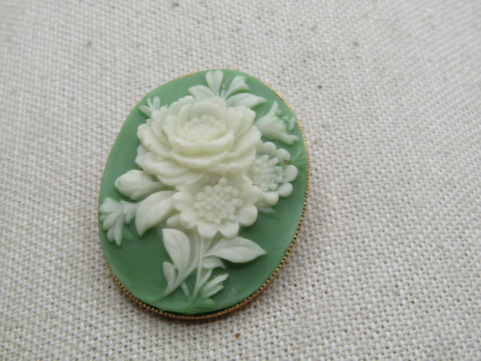 Vintage Green Floral Cameo Brooch, 1960's: Vintage Green Floral Cameo Brooch, 1960's. Raised white floral bossoms over a background of green. It is gold tone, oval and appx. 1.5" by 1.25". Very good condition. The white blossoms are faux