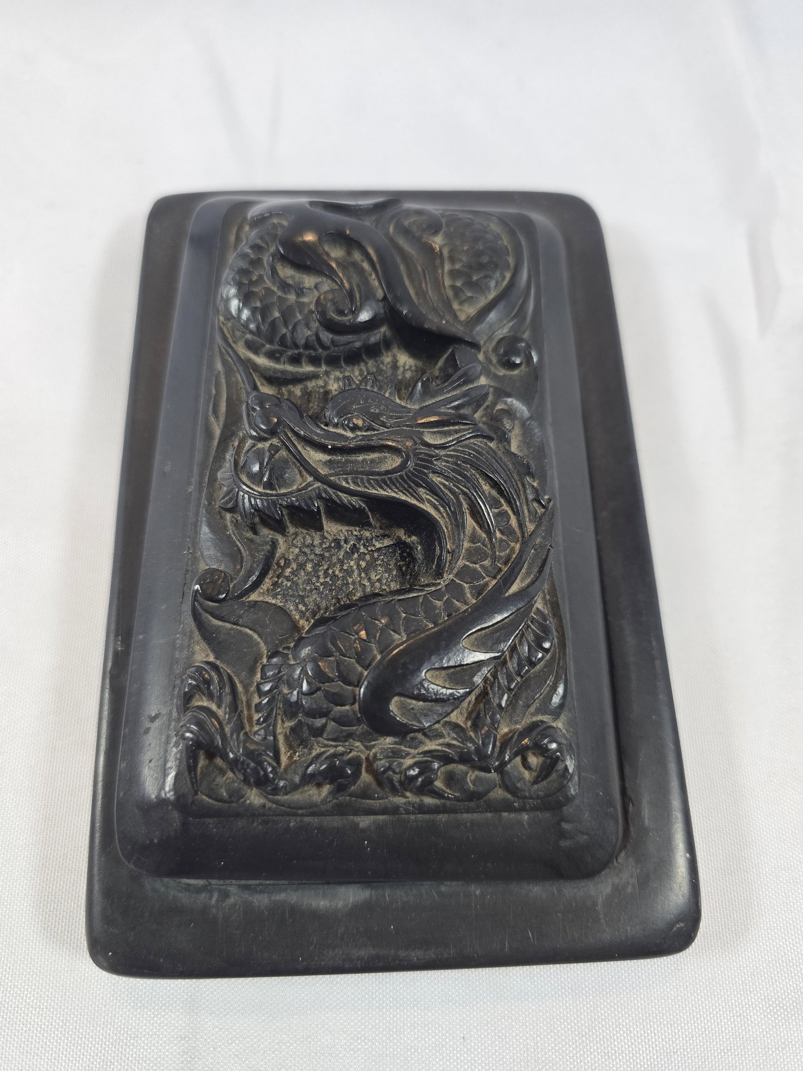 Carved Soapstone Box with Dragon Motif: A rectangular carved soapstone box, likely of East Asian origin (possibly Chinese or Japanese), featuring a complex relief carving of a dragon amidst clouds or waves on the lid. The carving style