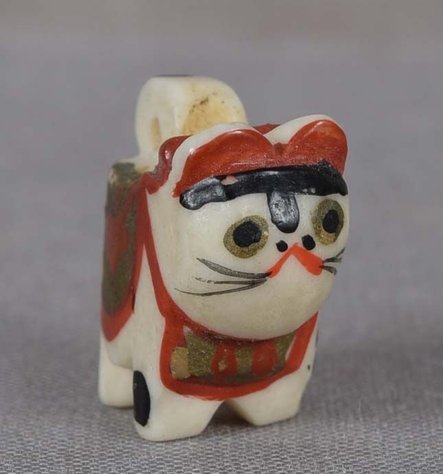 19c OJIME netsuke slide TOY DOG INU HARIKO: Late 19th century bone ojime (slide bead for tightening the cord going from netsuke to inro) carved as a toy dog (inu hariko) with a loop for hanging with gold, red and black lacquer decoration. Inu h