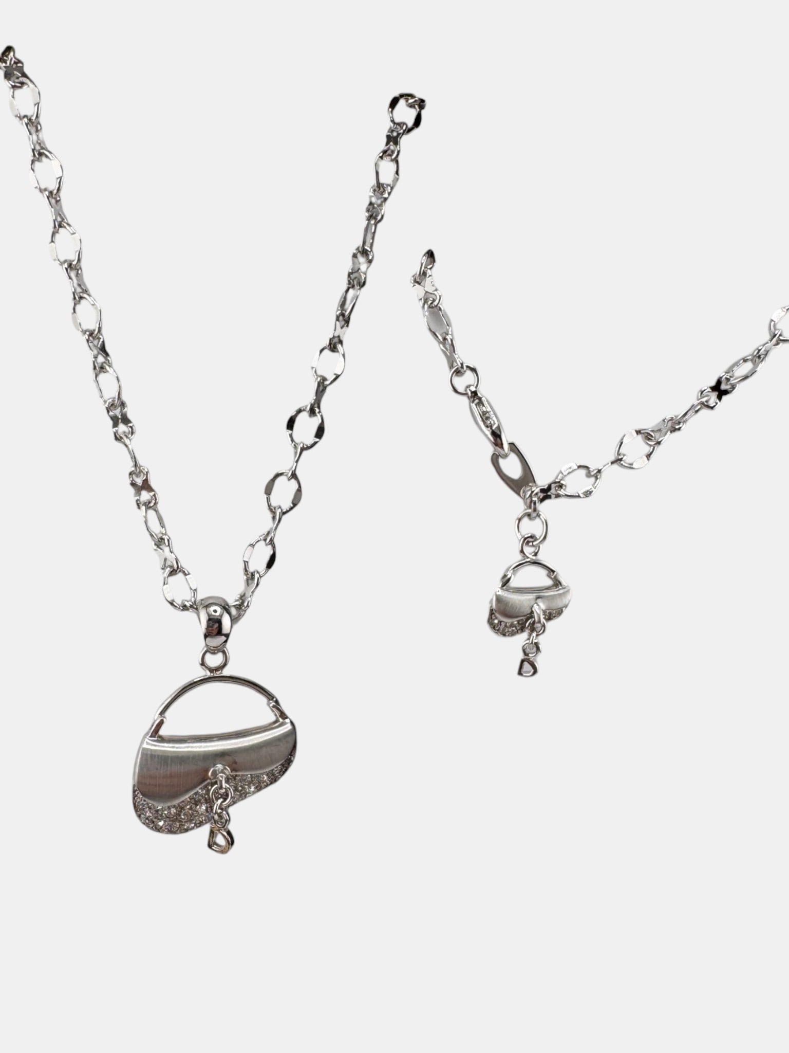 Silver Tone Purse Charm Necklace and Bracelet Set: This charming necklace and bracelet set features silver tone chains with novelty charms. The necklace and bracelet showcase a purse-shaped charm, accented with pave-set cubic zirconia, and a small