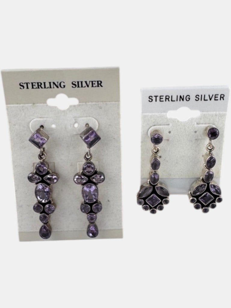 Vintage Sterling Silver Earrings: A lot featuring two distinct pairs of sterling silver earrings, each adorned with multiple faceted possibly amethyst gemstones. The first pair, designed as chandeliers, showcases a cascade of oval,
