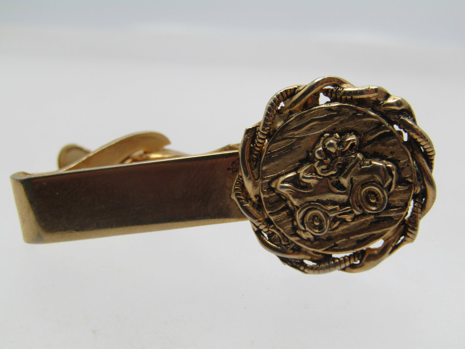 Vintage Model T/A Tie Clasp, 1950's-1960's: Vintage Model T/A Tie Clasp, 1950's-1960's. Gold tone with a raised old time car in the center of a textured round twisted gold tone setting. The decorative part is appx. 3/4" wide and tall and it