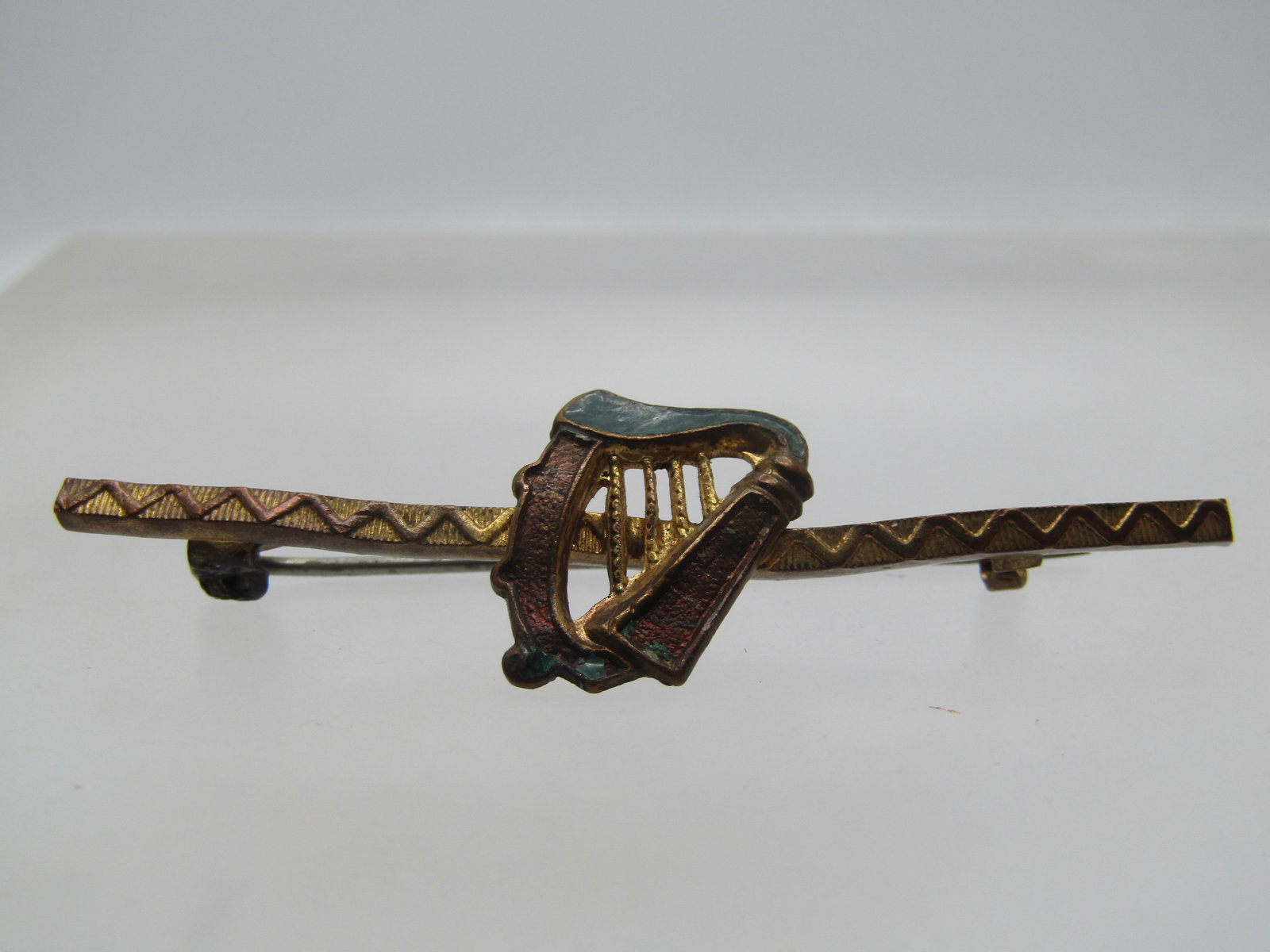 Antique Harp Bar Brooch, C-Clasp, 1920's: Antique Harp Bar Brooch, C-Clasp, 1920's. This has a raised zigzag design on the thin bar with a harp like instruments mounted on the center of the bar. It is appx. 5/8" tall and 1/2" wide at the