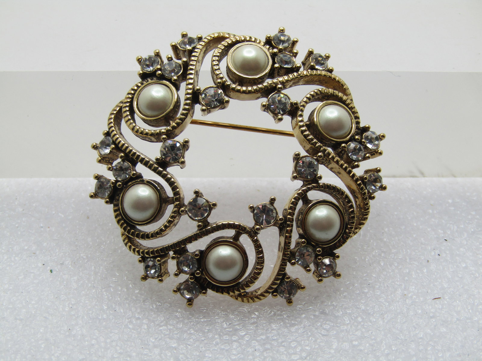 Vintage Monet Faux Pearl Rhinestone Brooch, 1960's-1980's, 1.75": Vintage Monet Faux Pearl Rhinestone Wreath Brooch, 1960's-1970's, 1.75". This is gold tone with a ridged swirled design around he faux pears moving around creating the wreath and with clear