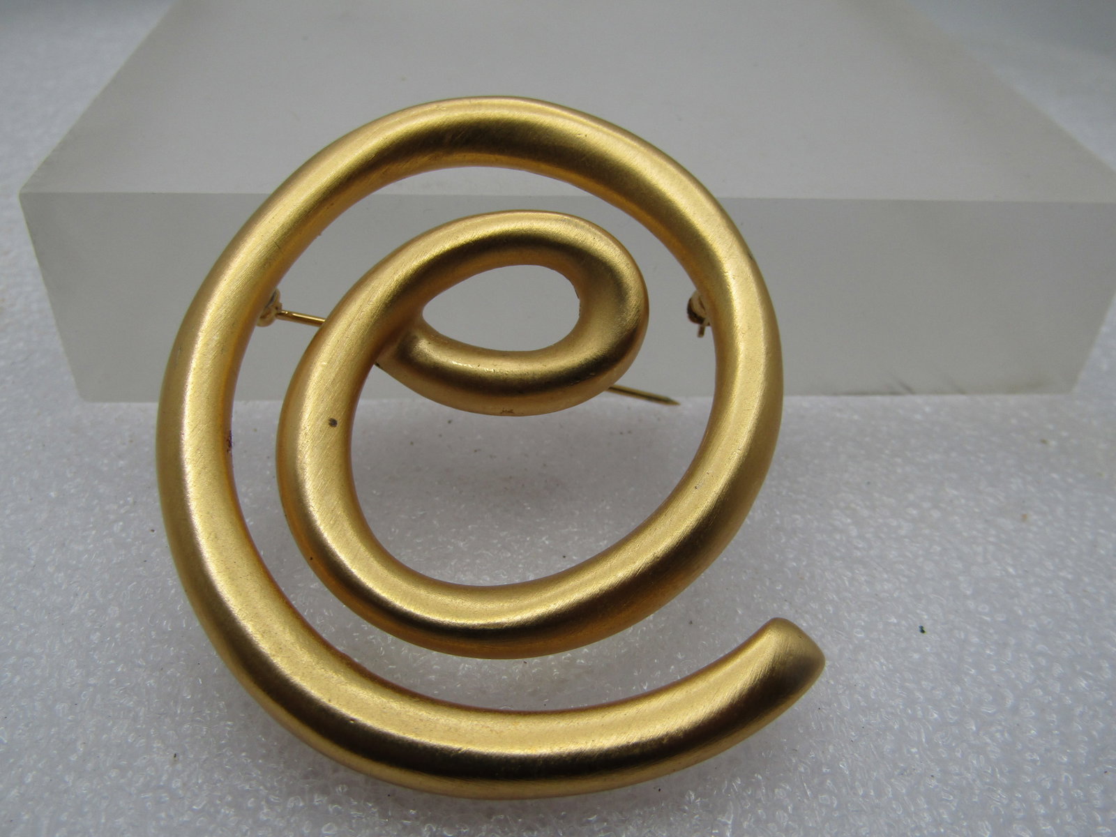 Vintage Gold Tone Spiral Brooch, 1980's. 2-1/3": Vintage Gold Tone Spiral Brooch, 1980's. 2-1/3" by 2.25". Satiny finish with an offset center that has a oval like design from which the spiral moves outward. it has a copyright mark but no name. 