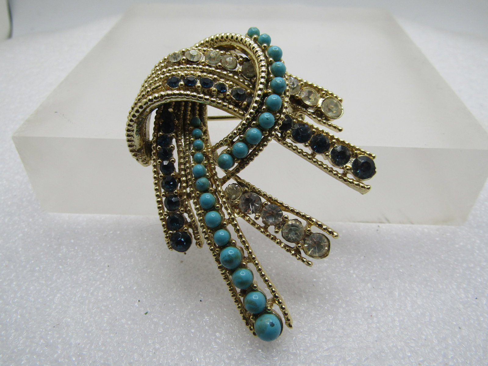Vintage Faux Turquoise Rhinestone Swoop Brooch, 1960's-1970's: Vintage Faux Turquoise Rhinestone Swoop Brooch, 1960's-1970's. Gold tone textured frame double strand that loops over itself creating staggered tails and a looped bow on top. Graduated faux