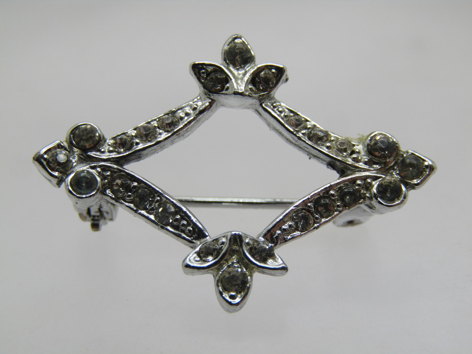 Vintage Rhinestone Open Rhinestone Brooch, Diamond Shape, 1960's: Vintage Rhinestone Open Rhinestone Brooch, Diamond Shape, 1960's. Silver tone and appx. 1-1/8" wide and 7/8" tall with triangular, fleur-de-lis-ish accents at the points with rhinestones set in those