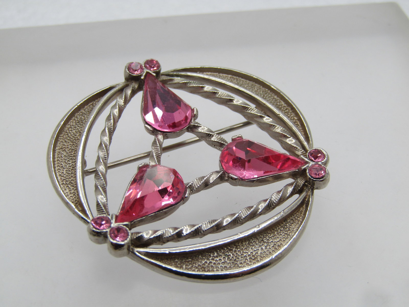 Vintage Pink Rhinestone Brooch, Mod Design, 1960's-1970's: Vintage Pink Rhinestone Brooch, Mod Design, 1960's-1970's. Textured and smooth silver tone finish with twisted accents and recessed curved frame. There are three pear shape pink rhinestones that are a