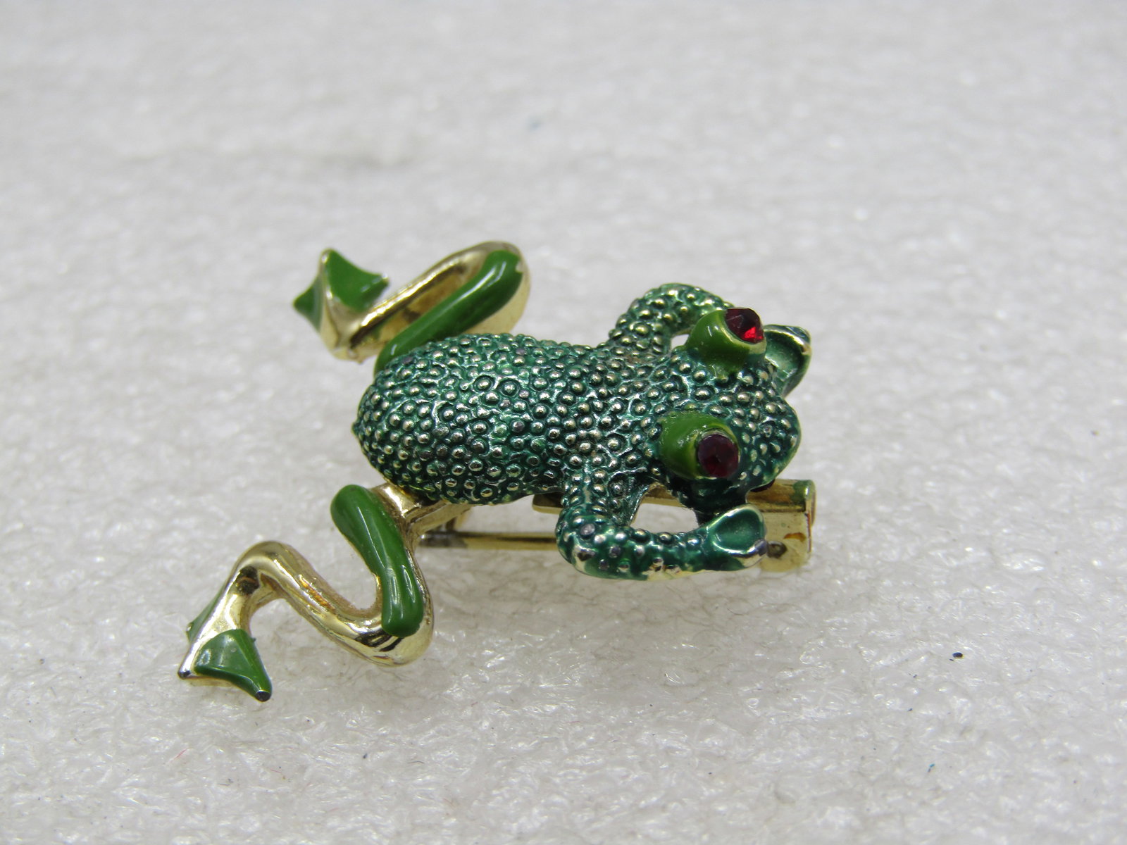 Vintage Enameled Articulated Frog Brooch, Red Rhinestone Eyes: Vintage Enameled Articulated Frog Brooch, Red Rhinestone Eyes, Green and gold tone with textured body. 1.25" long with back legs that move from side to side. 1960's-1970's. Not signed by the maker. Ve