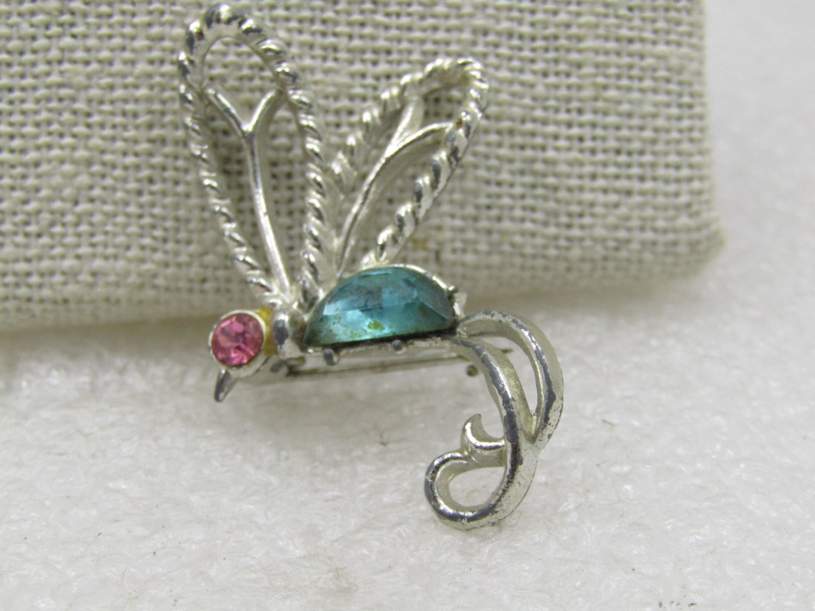 Vintage Stylized Hummingbird Rhinestone Brooch, 1960's: Vintage Stylized Hummingbird Rhinestone Brooch, 1960's. Silver tone body with a pink rhinestone head and an aqua body with raised textured and smooth wings and a curled tail. It is nearly 1.75"