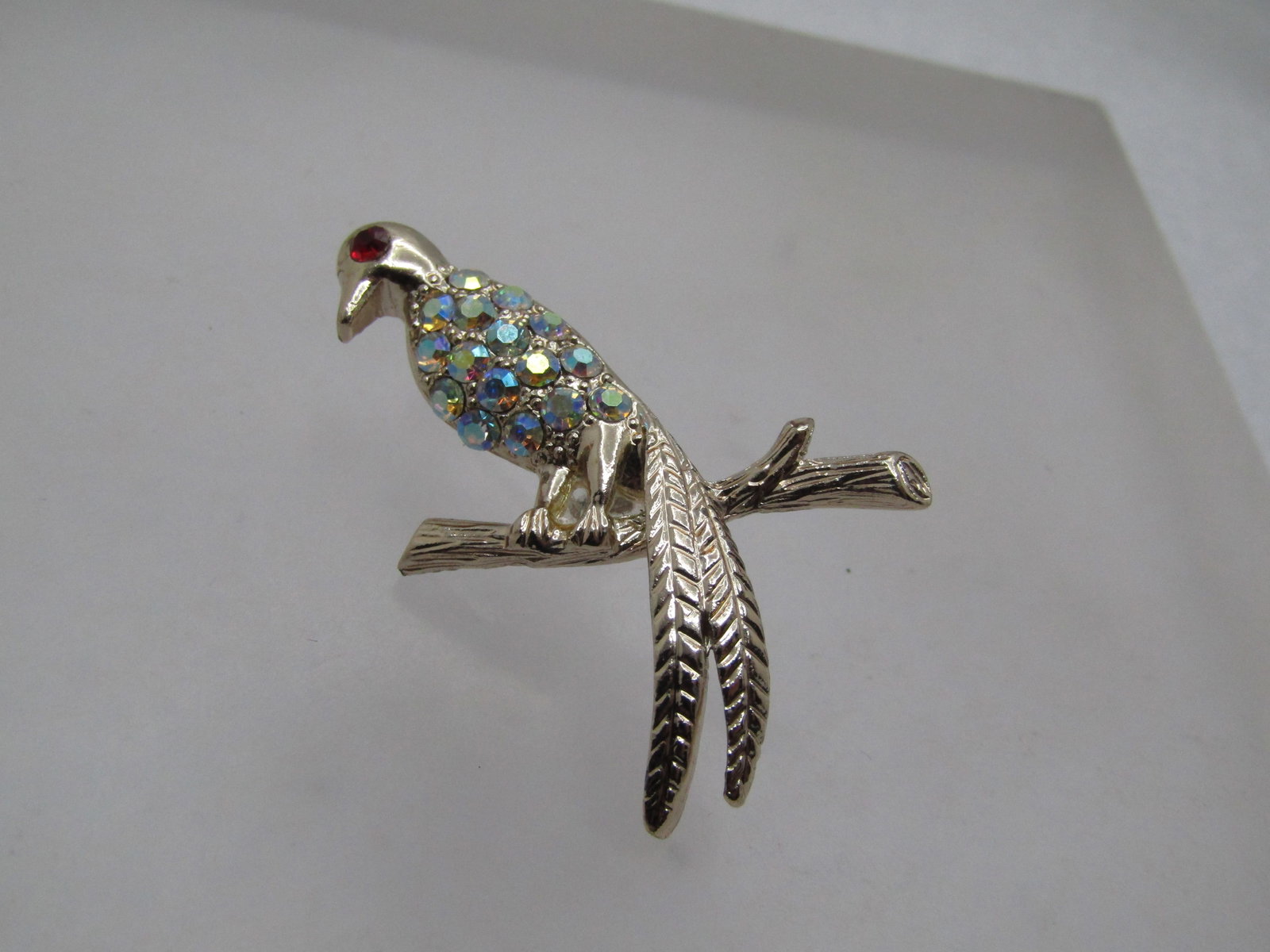 Vintage Rhinestone Bird on Branch Brooch, 1960's: Vintage Rhinestone Bird on Branch Brooch, 1960's. Silver tone with red rhinestone eye, aurora borealis rhinetones in the body, long tail and sitting on a branch, textured wood finish on the brach and