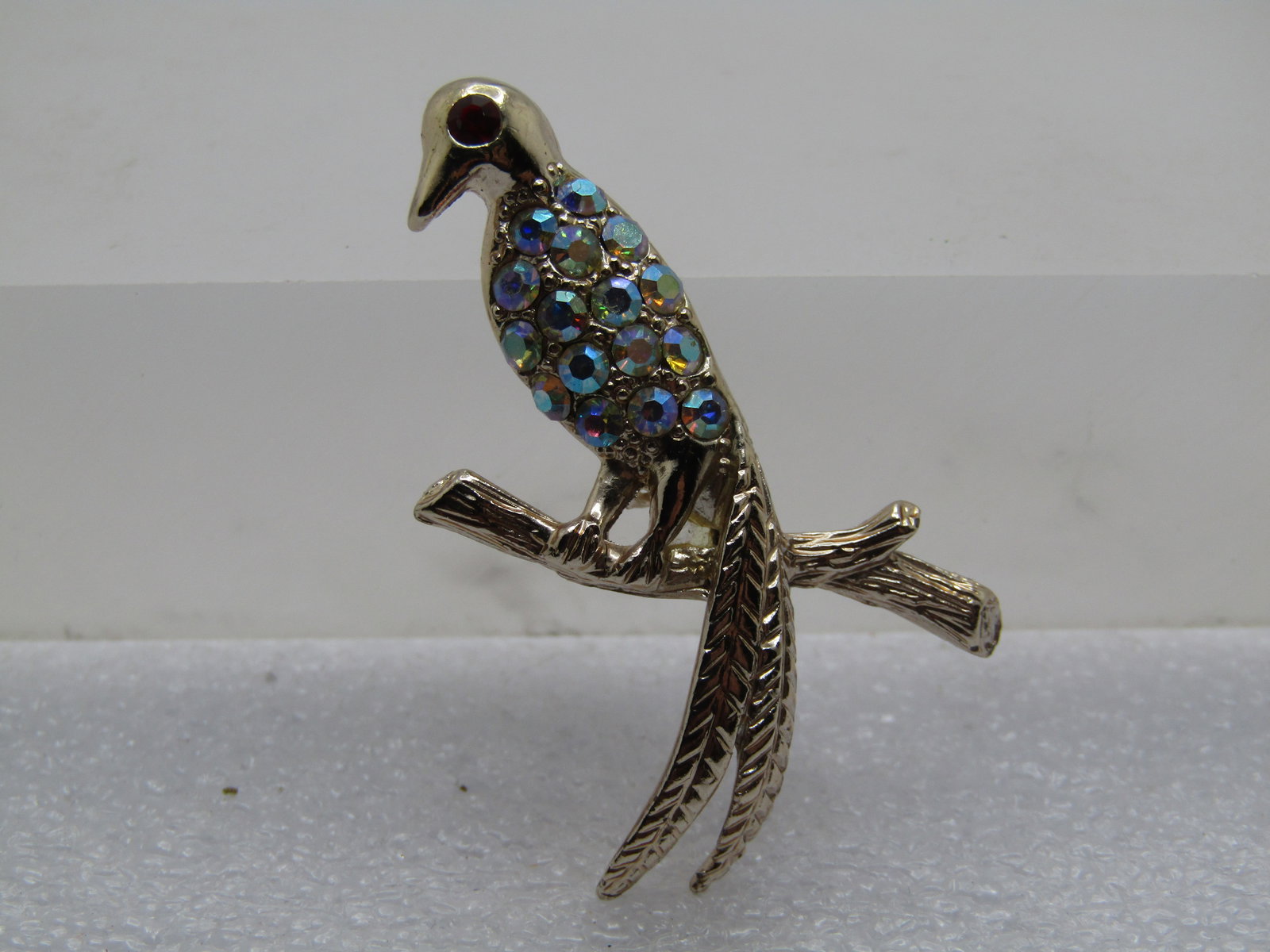 Vintage Rhinestone Bird on Branch Brooch, 1960's: Vintage Rhinestone Bird on Branch Brooch, 1960's. Silver tone with red rhinestone eye, aurora borealis rhinetones in the body, long tail and sitting on a branch, textured wood finish on the brach