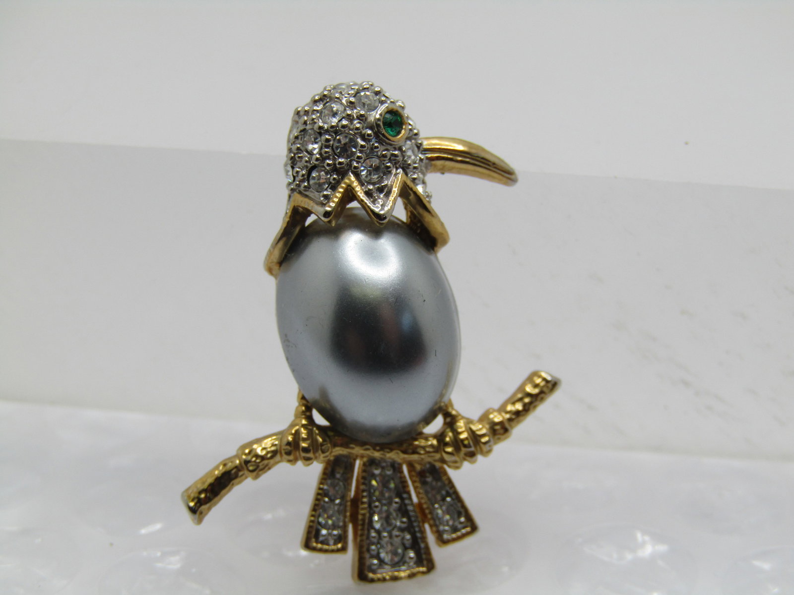 Vintage Faux Pearl & Rhinestone Bird Brooch, on Branch, 1980's: Vintage Faux Pearl & Rhinestone Bird Brooch, on Branch, 1980's. SIlvery faux Tahitian pearl torst with pave set clear rhinestone tail and head and green rhienstone eye. Gold tone branch, legs, beak an