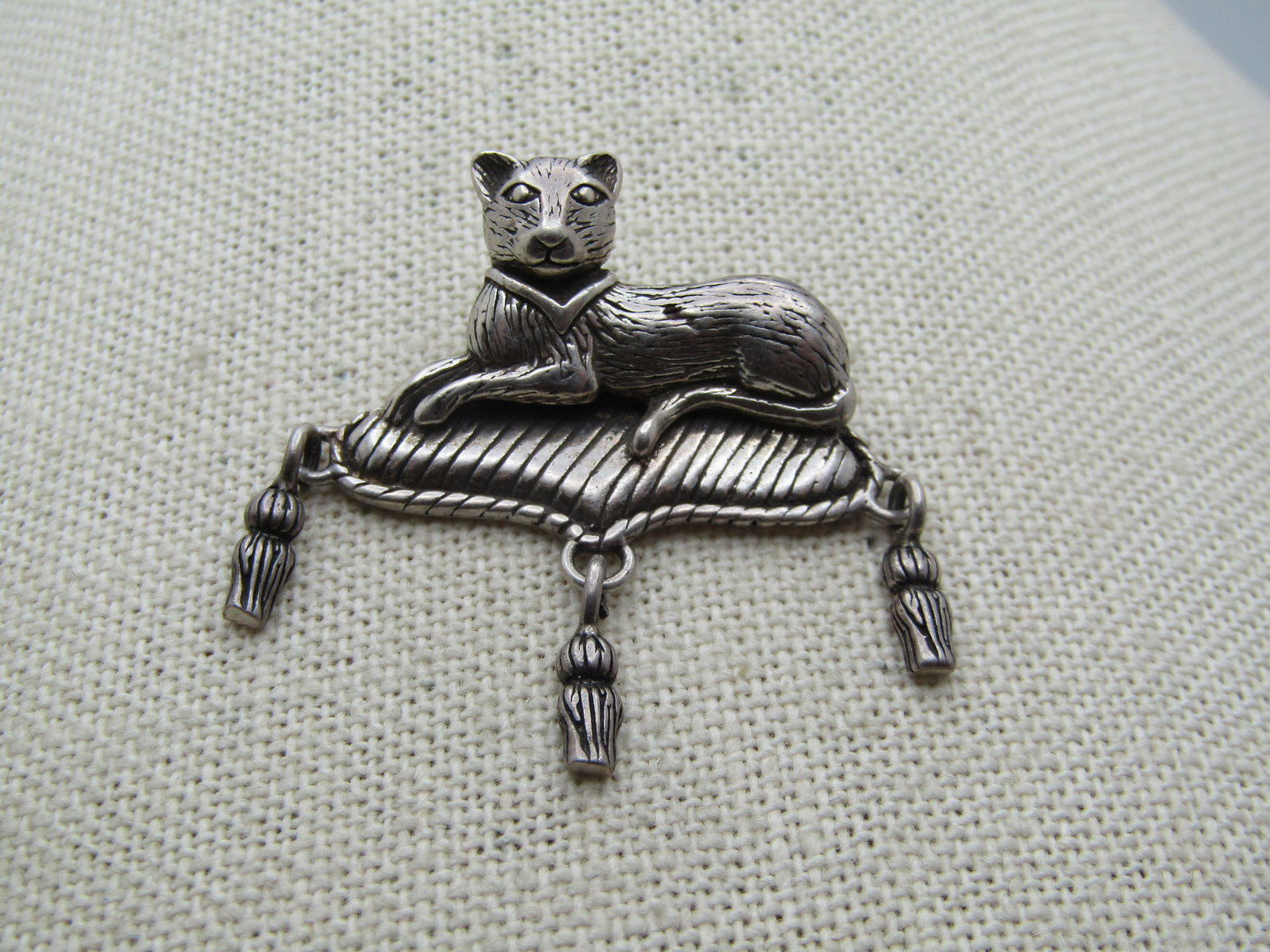 Vintage Sterling Cat on Cushion Brooch, 1980's-1990's, Jezlaine.: Vintage Sterling Cat on Cushion Brooch, 1980's-1990's. Very cute tasseled cushion with a regal-looking resting cat. Nice detail. It tests as sterling with a weight of appx. 9.43 gr. It is 1.5"