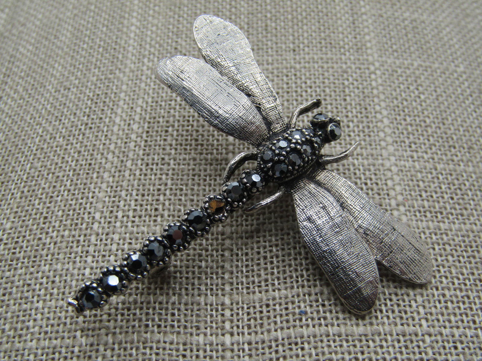 Vintage Black Rhinestone Dragonfly Brooch, 1980's-1990's: Vintage Black Rhinestone Dragonfly Brooch, 1980's-1990's. Silver tone with textured wings and shimmery black stones with aurora borealis shimmer. The brooch is appx. 1.75" long and 2" wide at the