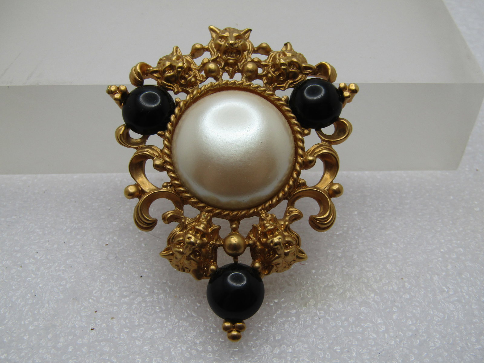 Vintage Faux Pearl Lion Heads Brooch, Signed Avon, 1980's: Vintage Faux Pearl Lion Head Brooch,s Signed Avon, 1980's. Center 1" faux pearl with three 8mm half round black cabochon accents. It is papx. 2.25" tall and 1.75" wide. Gold beaded accents too. 
