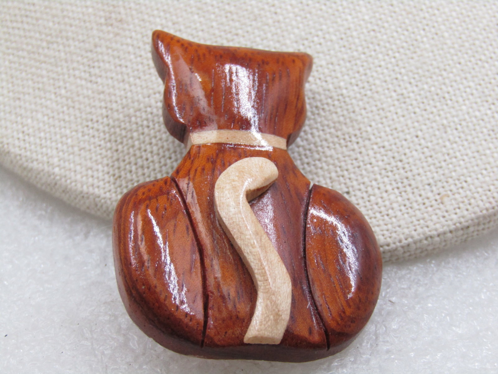 Hand Made Carved Wooden Cat Brooch, Two-Tone, 2": Hand Made Carved Wooden Cat Brooch, Two-Tone, 2" tall 1.5" wide. Glossy finish with the tail curled up it's back and set raised on it's back. The color is a lighter wood to and it is inlaid into the