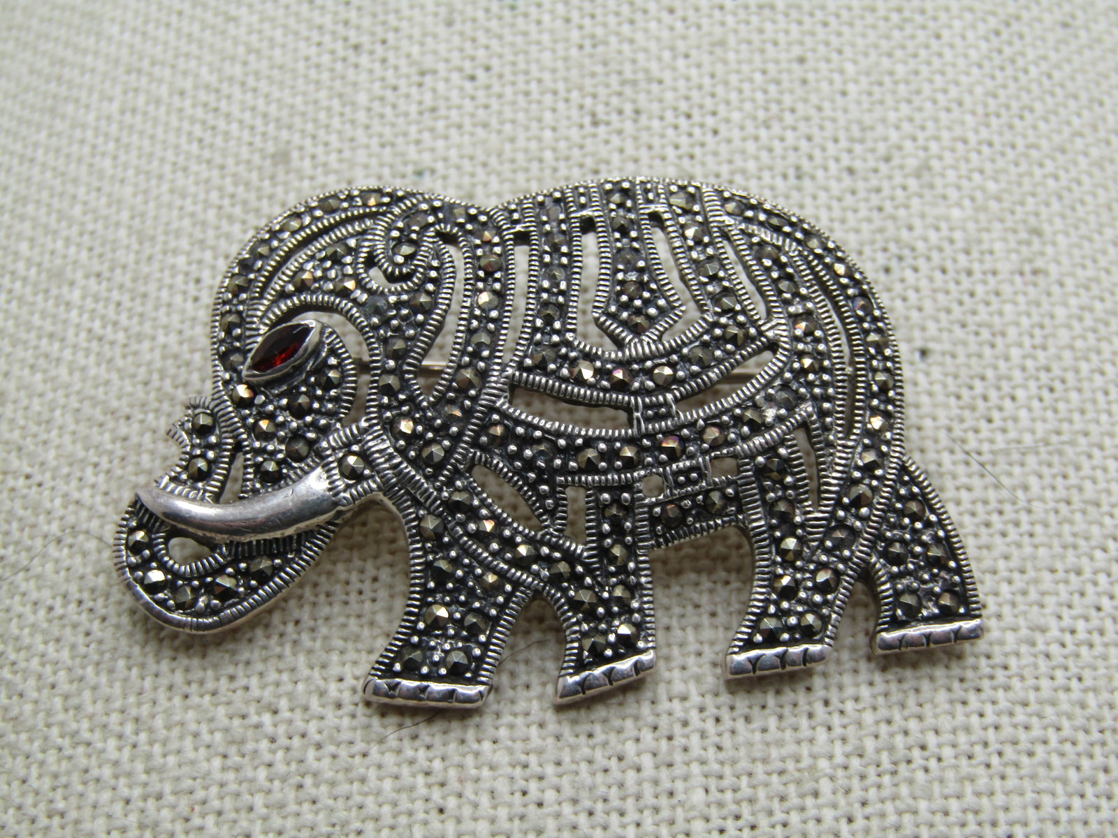 Vintage Sterling Marcasite Elephant Brooch, Garnet Eye, 1980's: Vintage Sterling Marcasite Elephant Brooch, Garnet Eye, 1980's. It is appx. 2" wide by 1.25" tall. It has open work and it's body is created by pave set marcasites throughout with a smooth tusck