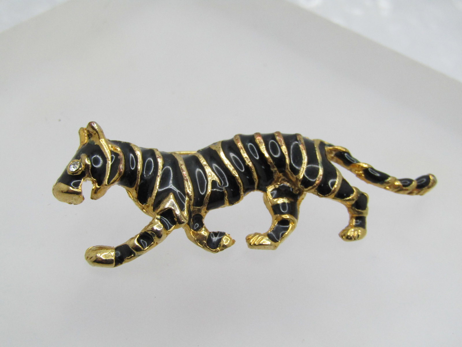 Vintage Enameled Tiger Brooch, Rhinestone Eye, 1980's: Vintage Enameled Tiger Brooch, Rhinestone Eye, 1980's. Gold tone setting with raised lines and black enameling between. Clear rhinestone eye. The tiger is appx. 2.25" wide and 7/8" tall. Locking clasp